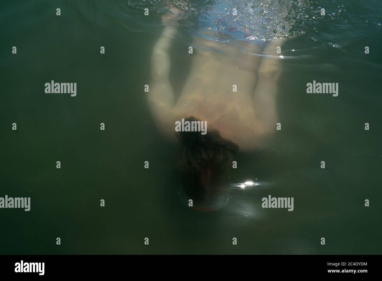 Young Man with Long Blonde Hair Swimming Underwater Stock Photo
