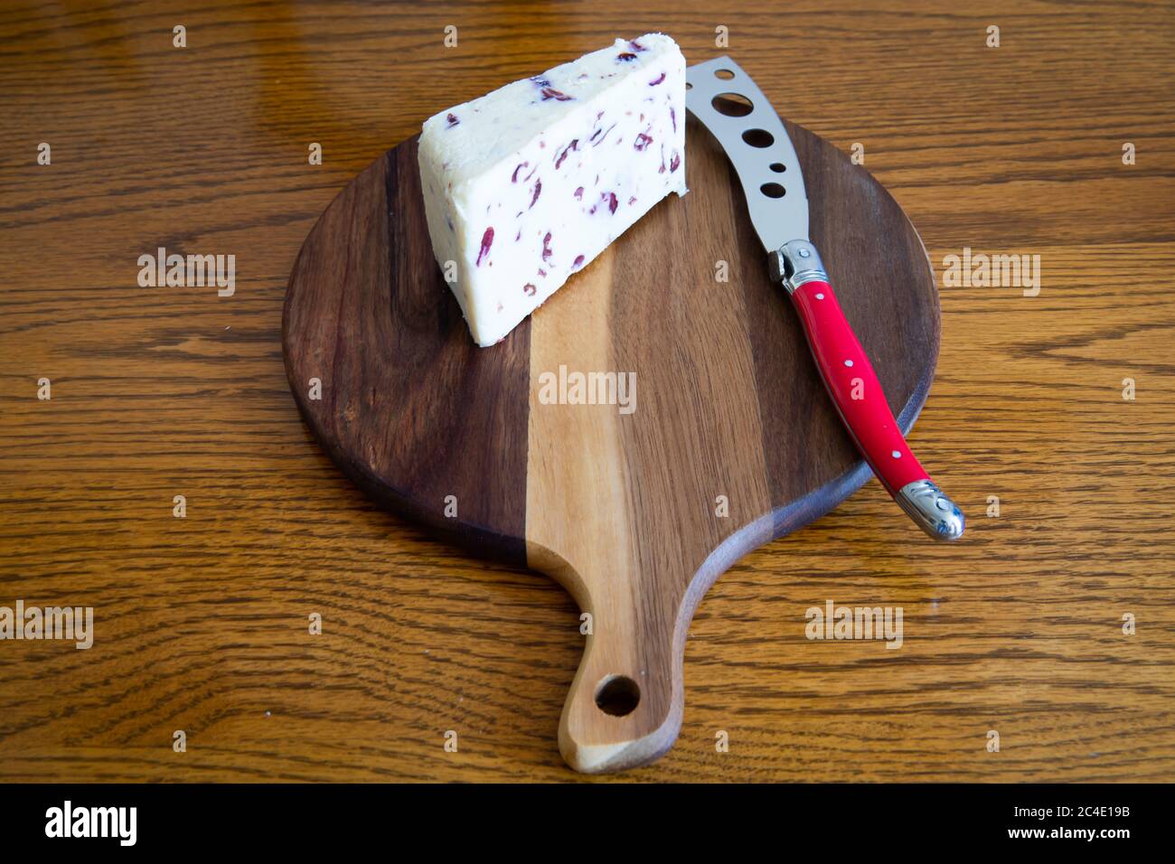 Wensleydale and Cranberry Cheese on a wooden cheeseboard with a red cheese knife Stock Photo
