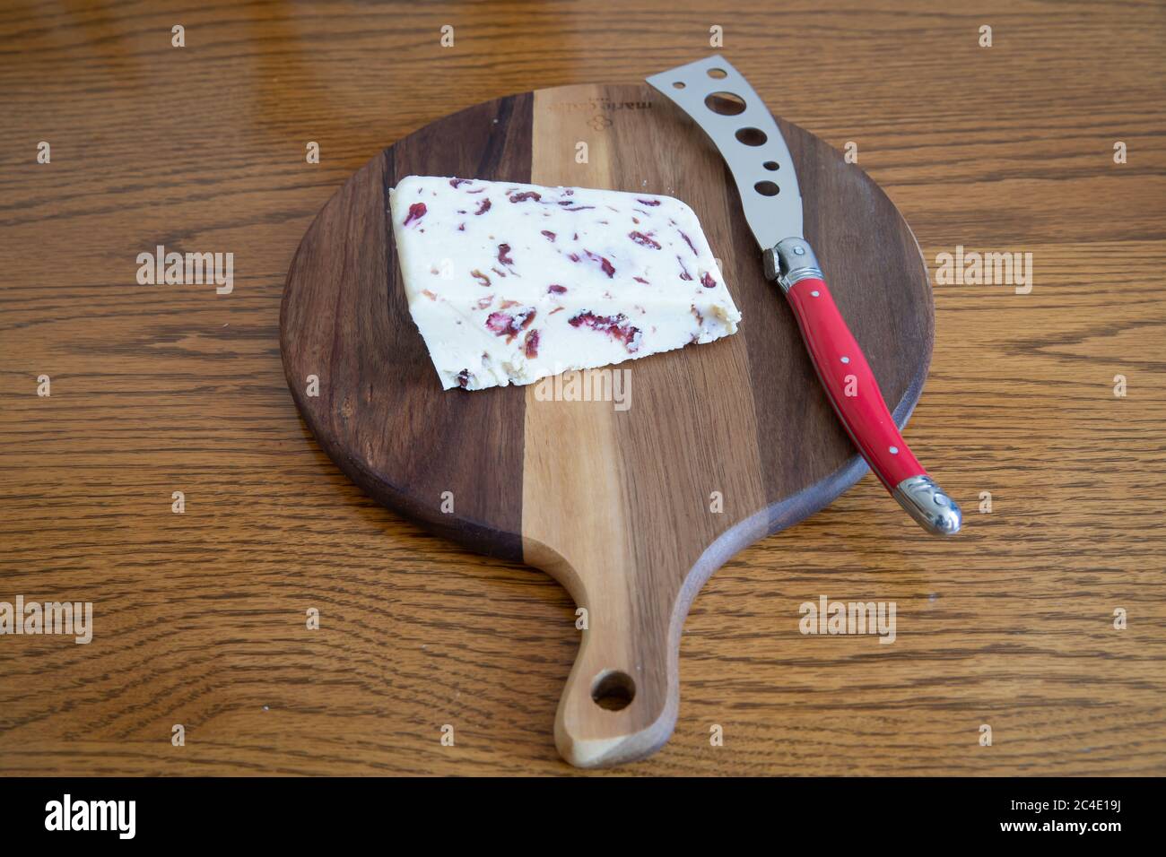 Wensleydale and Cranberry Cheese on a wooden cheeseboard with a red cheese knife Stock Photo