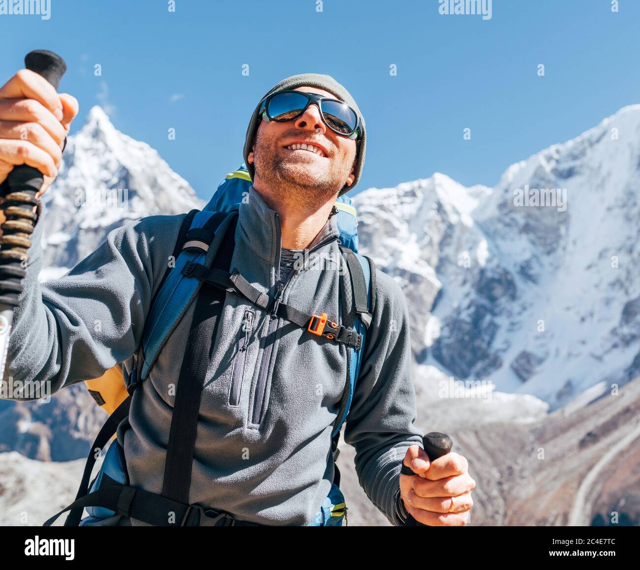 Portrait of smiling Hiker man on Taboche 6495m and Cholatse 6440m peaks background with trekking poles, UV protecting sunglasses. He enjoying mountain Stock Photo