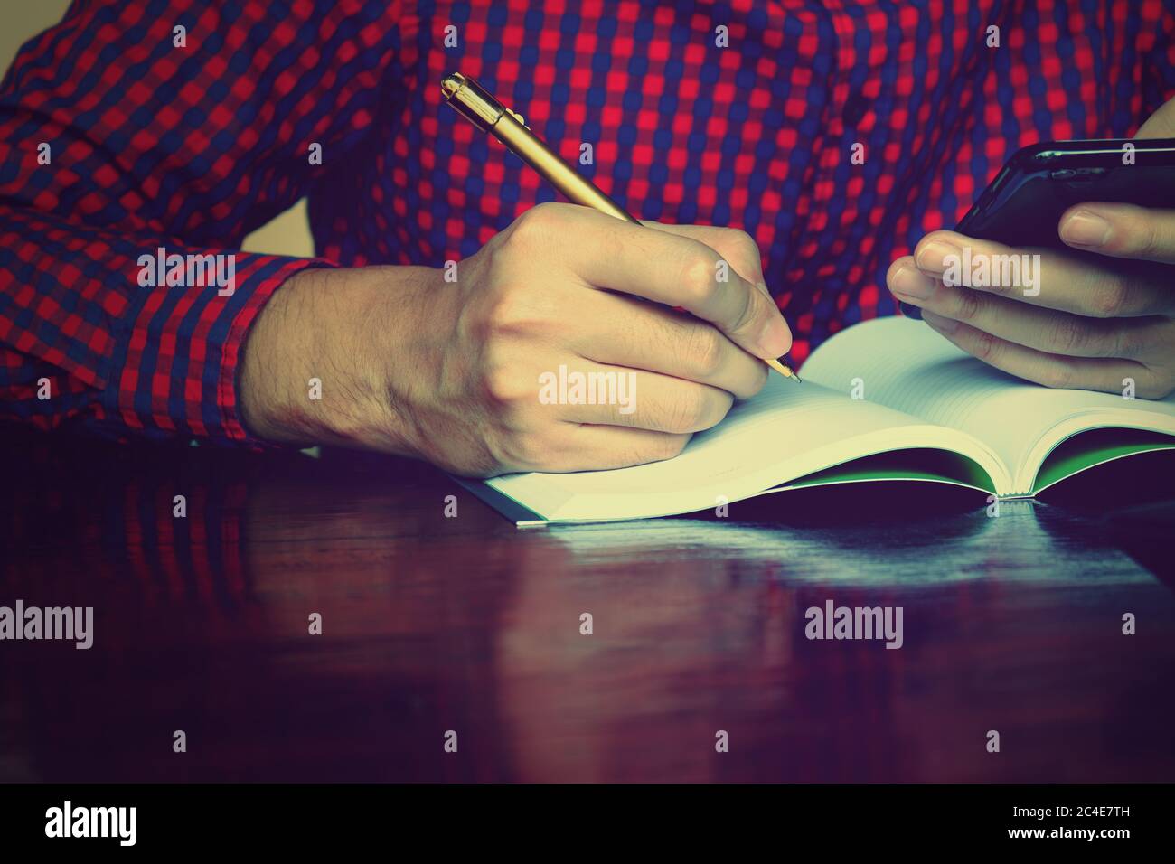 Young man writing on notebook about cost and holing phone using calculator in home office. Stock Photo