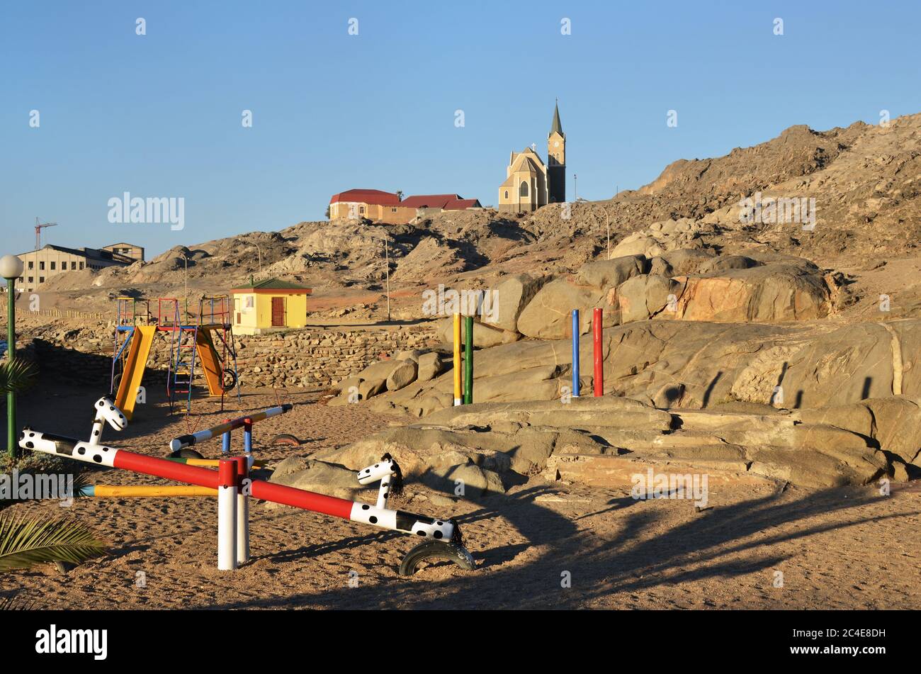 Public playground in the city of Luderitz. Bright colorful empty children's playground in the rock yard of a city district. Felsenkirche church on bac Stock Photo