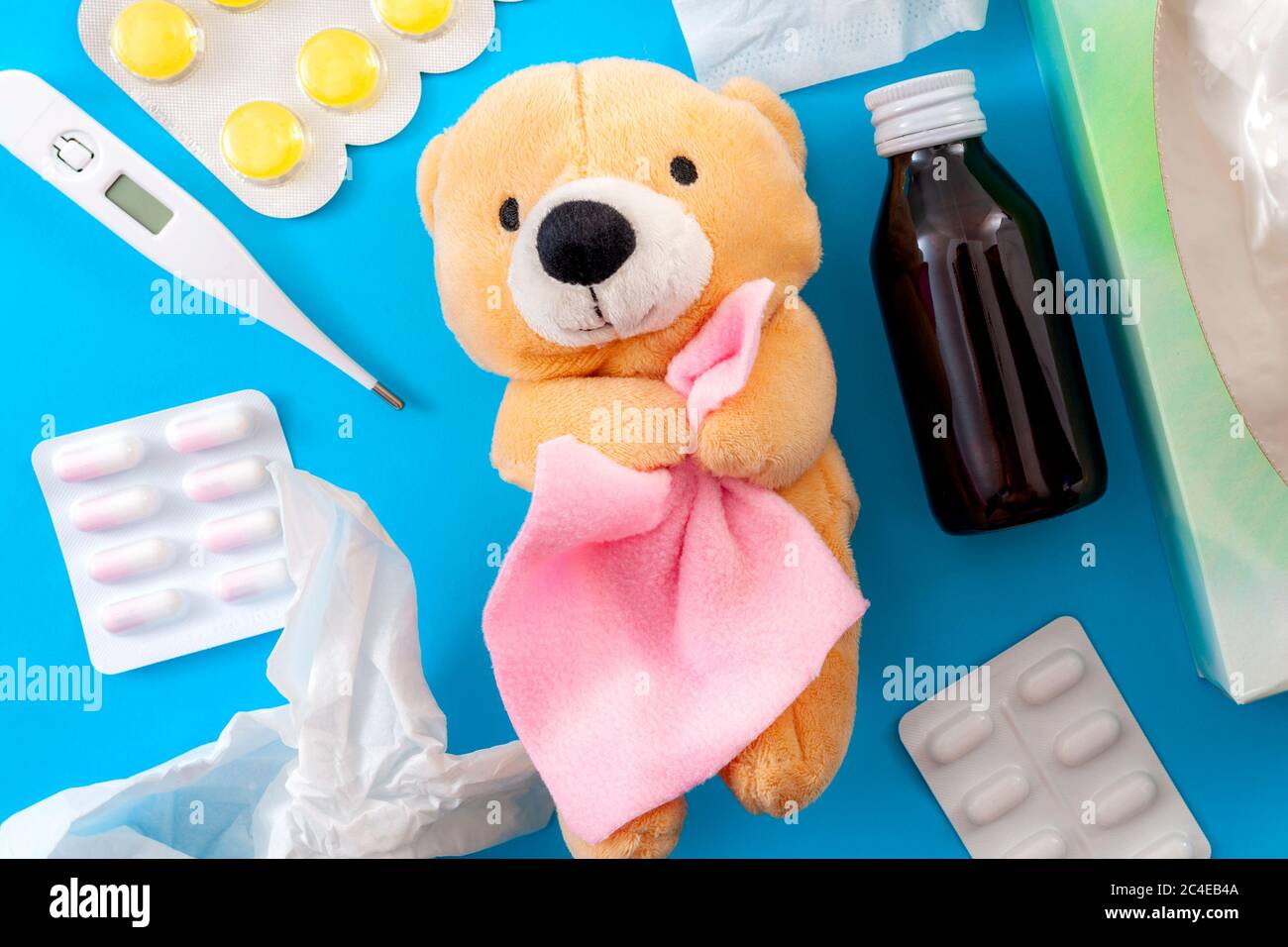 Cold and flu treatment and pediatrics medicine concept with a teddy bear holding a blanket surrounded by  a thermometer, bottle of cough syrup, sore t Stock Photo