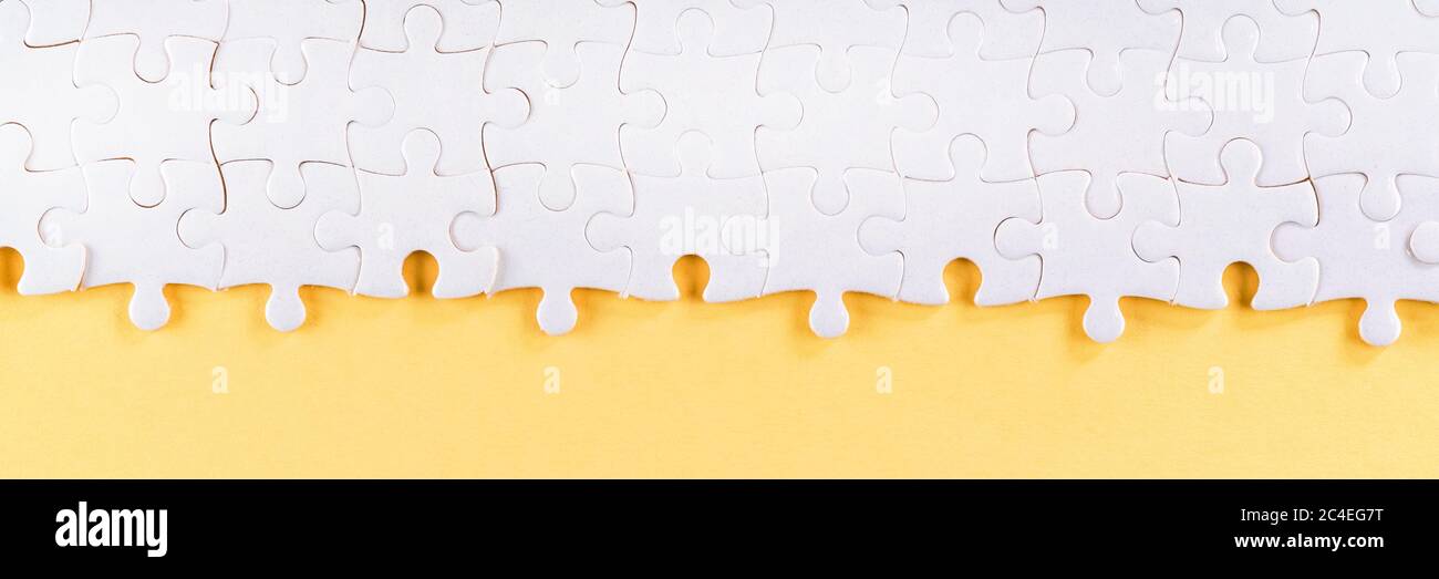 Assembled white jigsaw puzzle pieces on yellow. Long panoramic texture and background Stock Photo