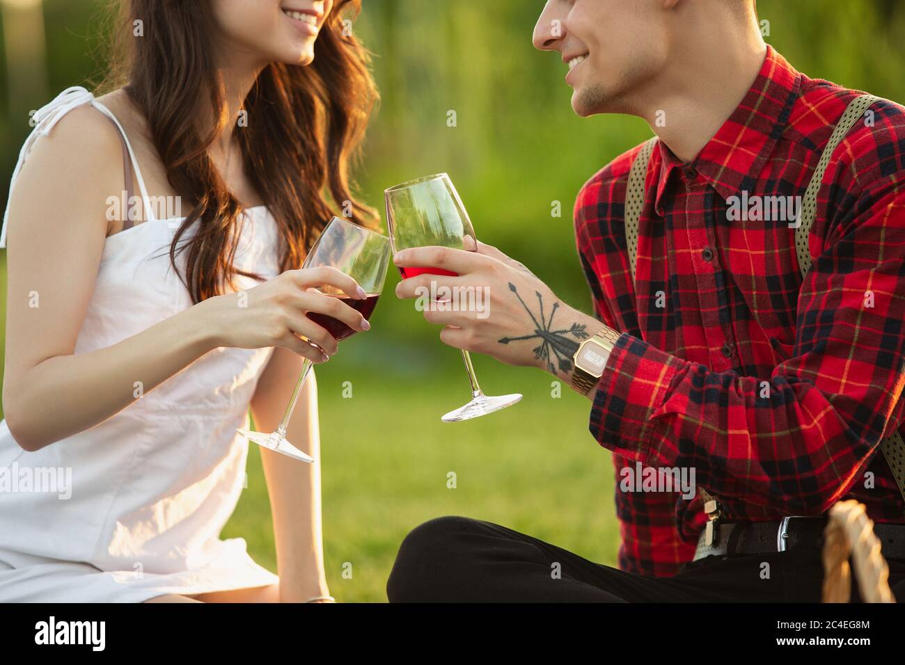Clinking glasses. Caucasian young couple enjoying weekend together in the park on summer day. Look lovely, happy, cheerful. Concept of love, relationship, wellness, lifestyle. Sincere emotions. Stock Photo