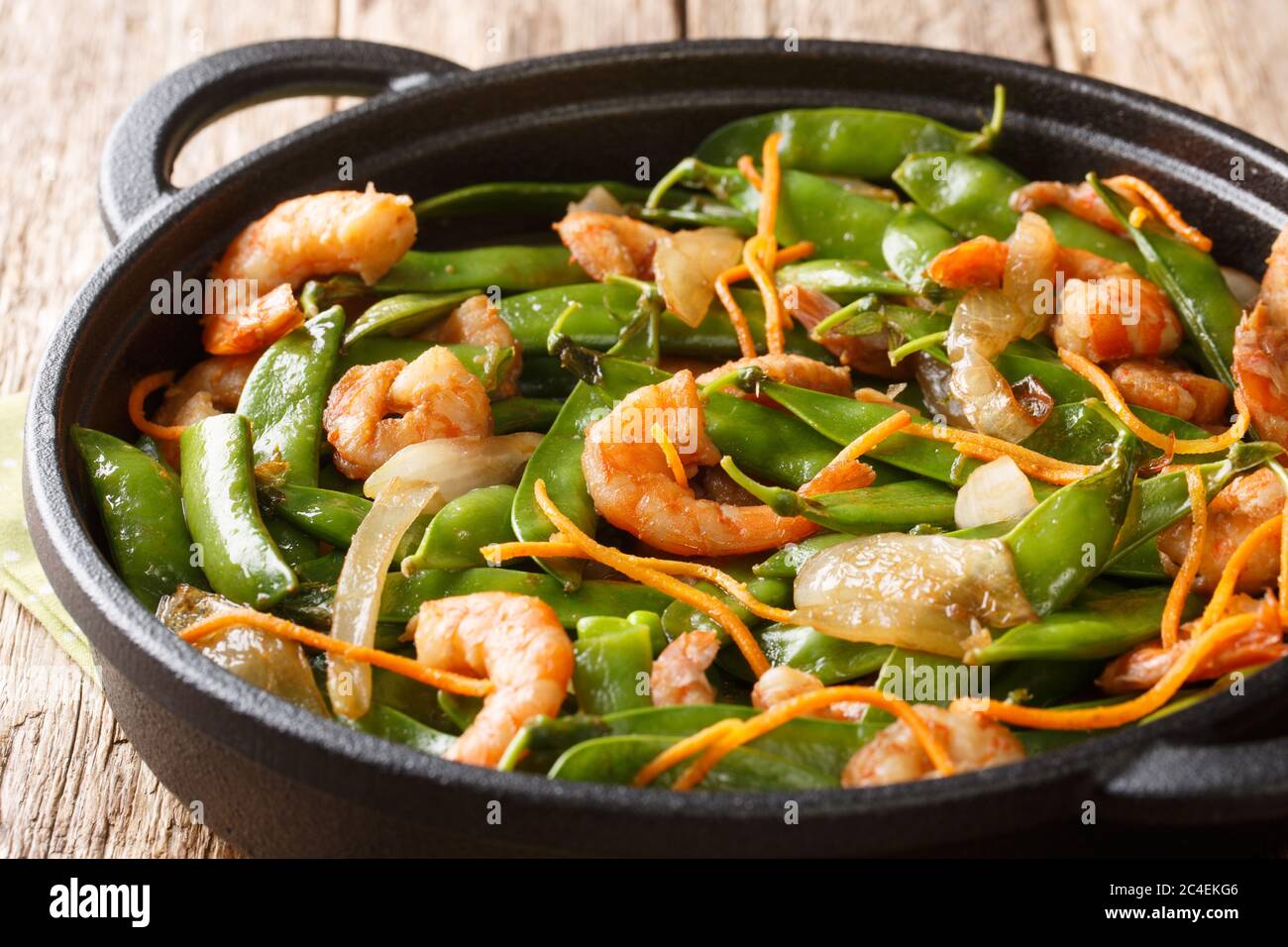 Fried shrimp recipe with onions, carrots and pods of snow peas close-up in a pan on the table. horizontal Stock Photo