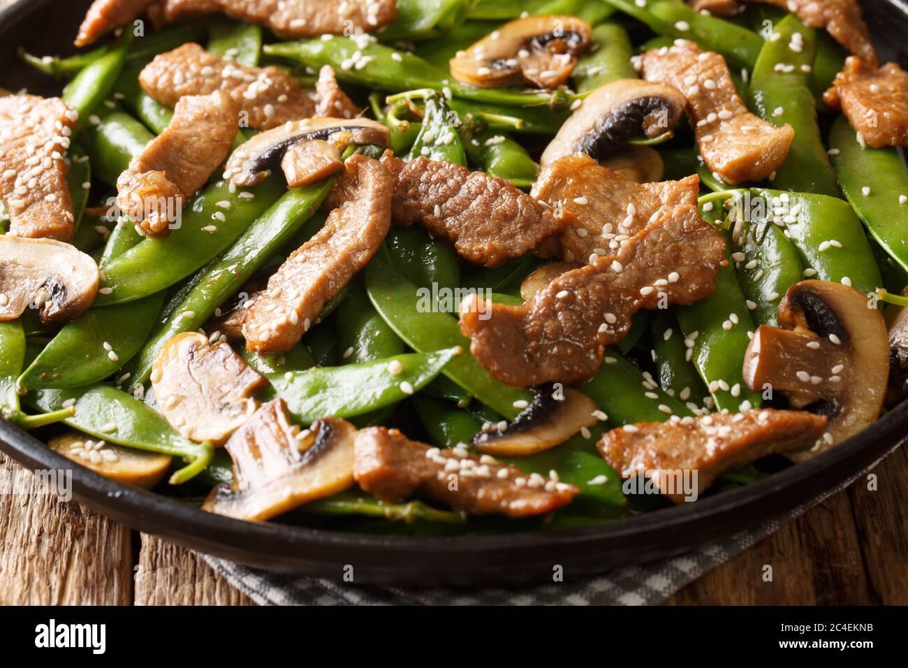 Asian stir-fried beef with mushrooms champignons and pods of green peas, sesame seeds close-up in a plate on the table. horizontal Stock Photo
