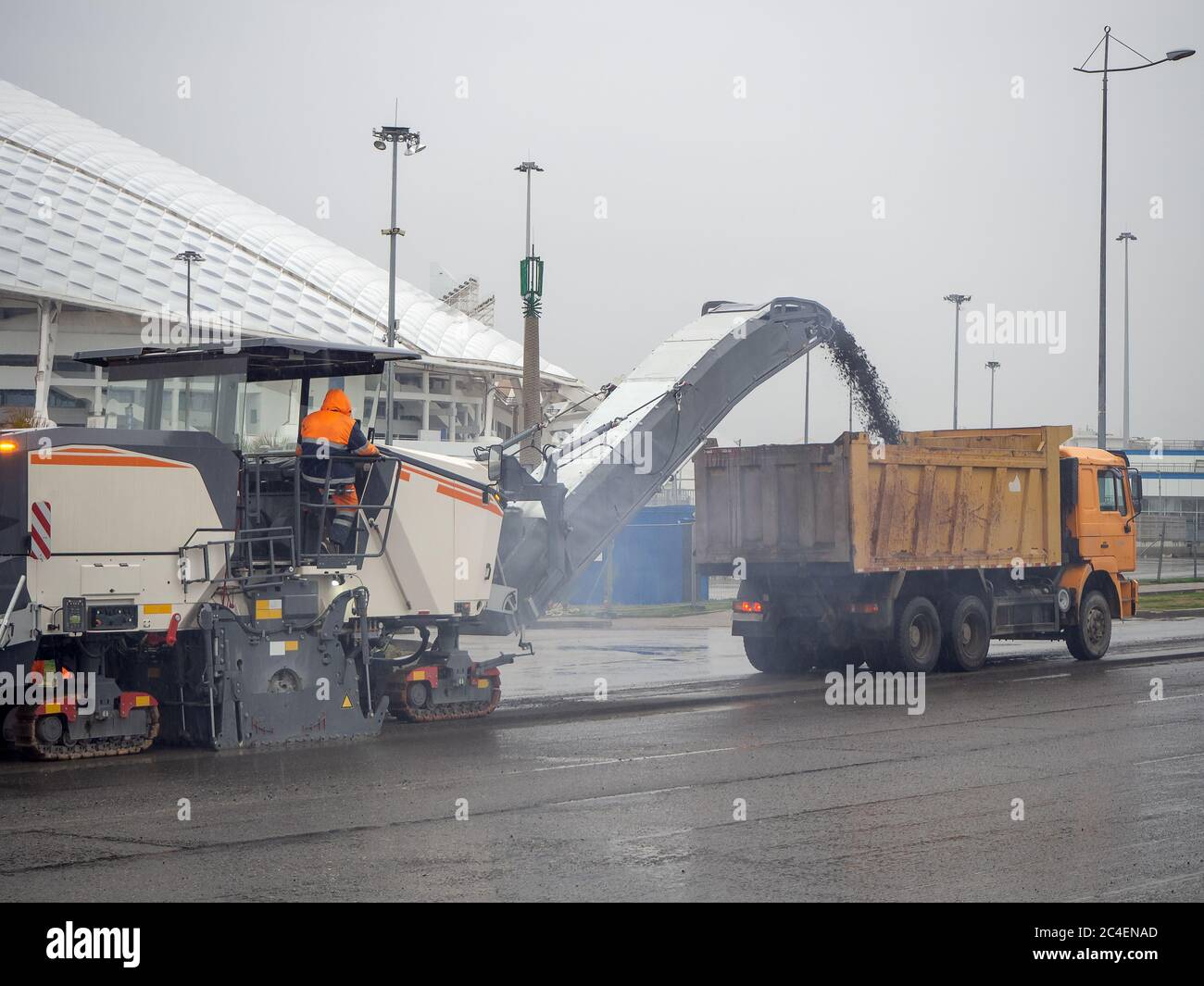 Cold milling machine loads crushed asphalt into a dump truck in cloudy weather Stock Photo