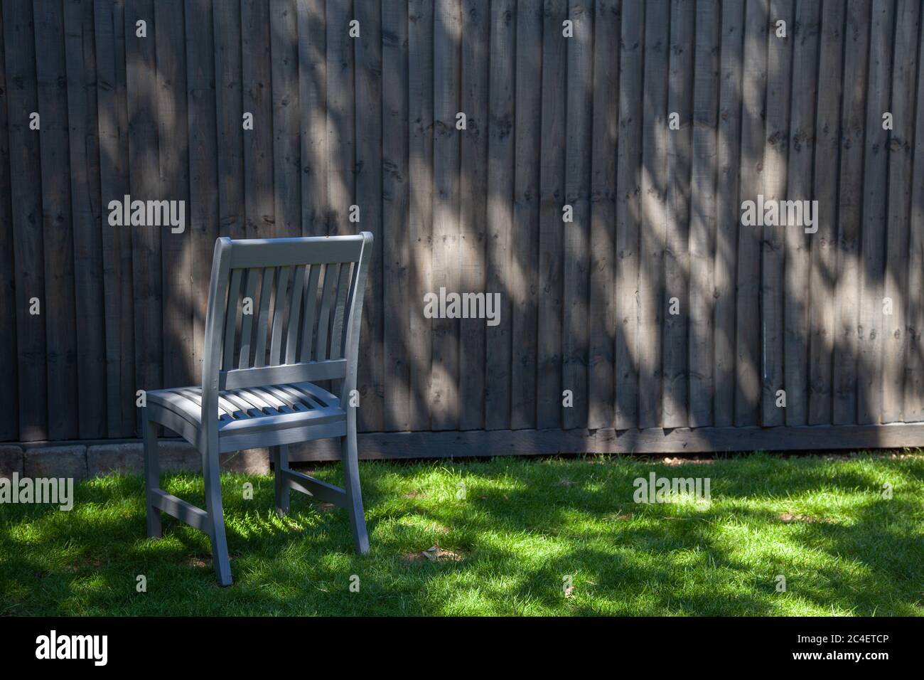 Grey garden chair, grey background, grey fence panel, shadows, grass