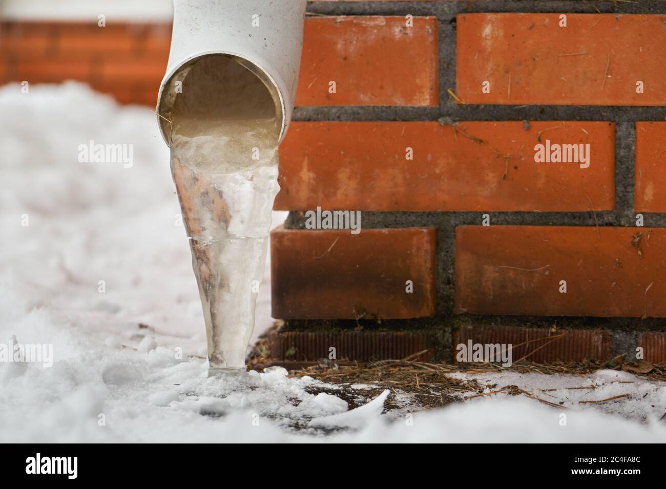Drain pipe with frozen stream of water near brick wall of a cottage