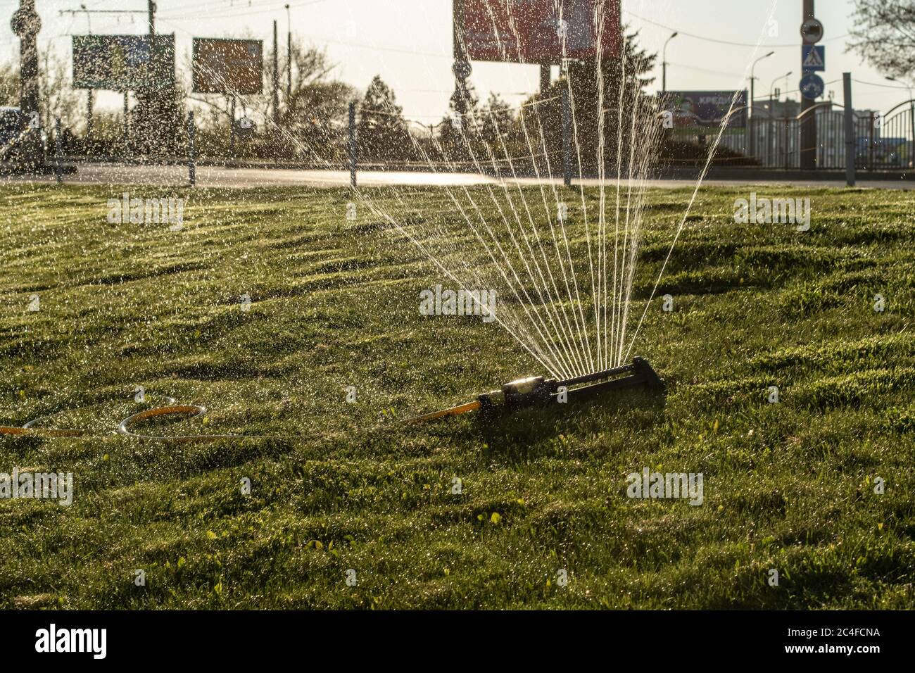 Portable, water efficient an oscillating sprinkler with metal arm sprays out a fan of water to the grass area in public streets. Watering lawn in city Stock Photo