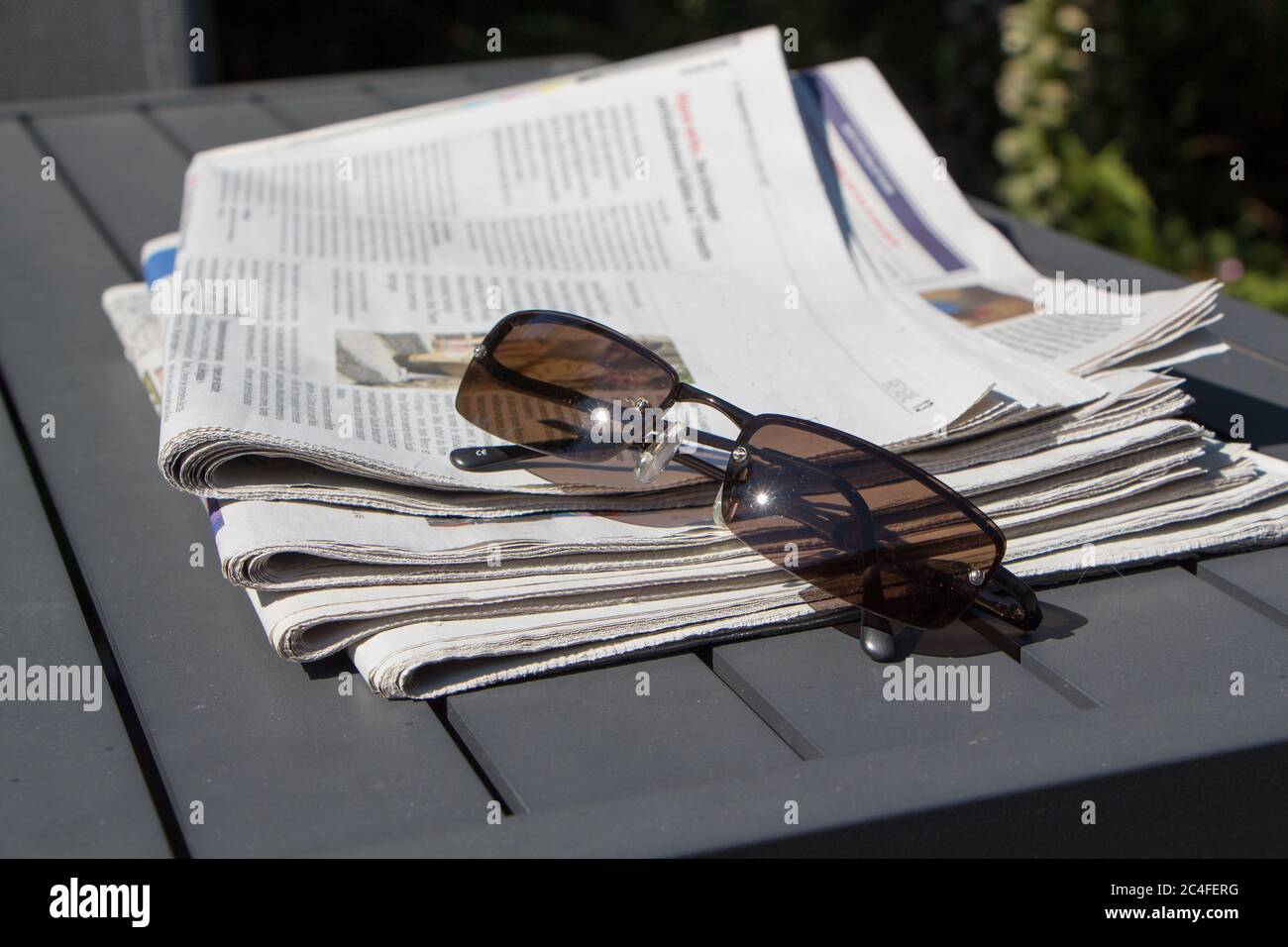 PRIMELIN - FRANCE, JULY 11 : Pile of newspapers and sunglasses on a table in a garden, July 11, 2018 Stock Photo