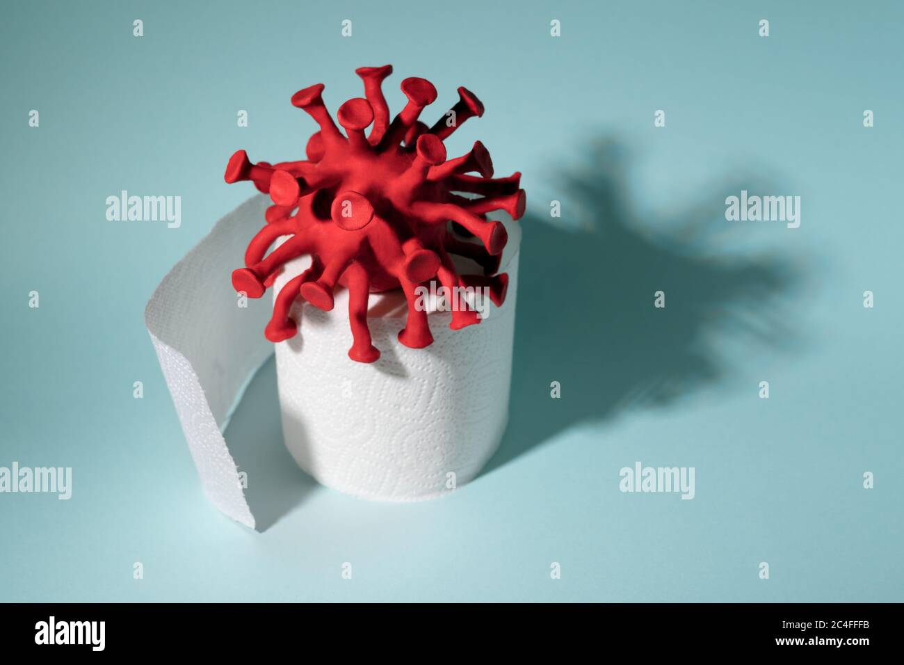 Red model of coronavirus sitting on the toilet paper roll. Concept of a
