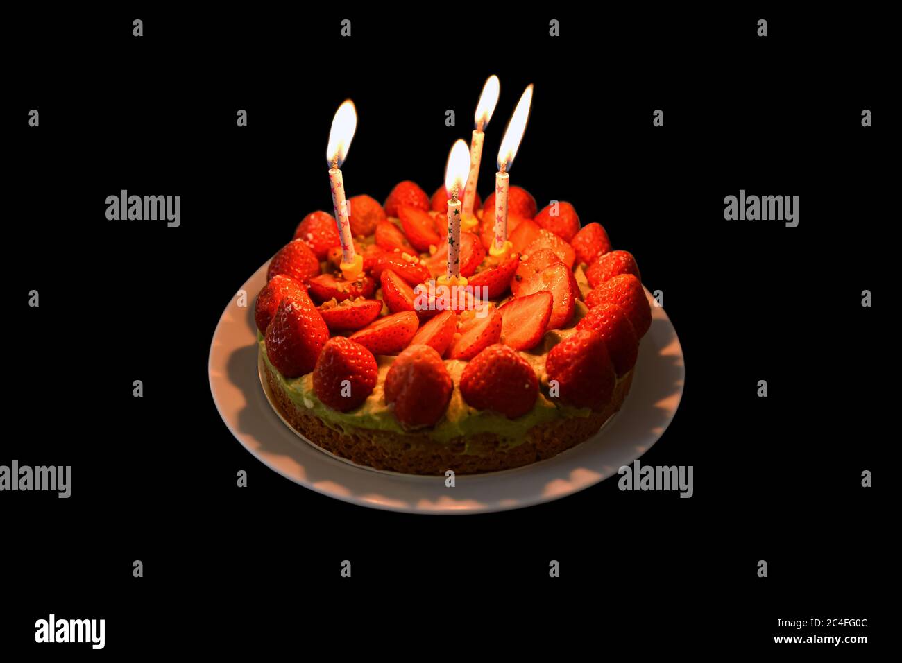 Strawberry birthday cake lit by four candles isolated on black ...