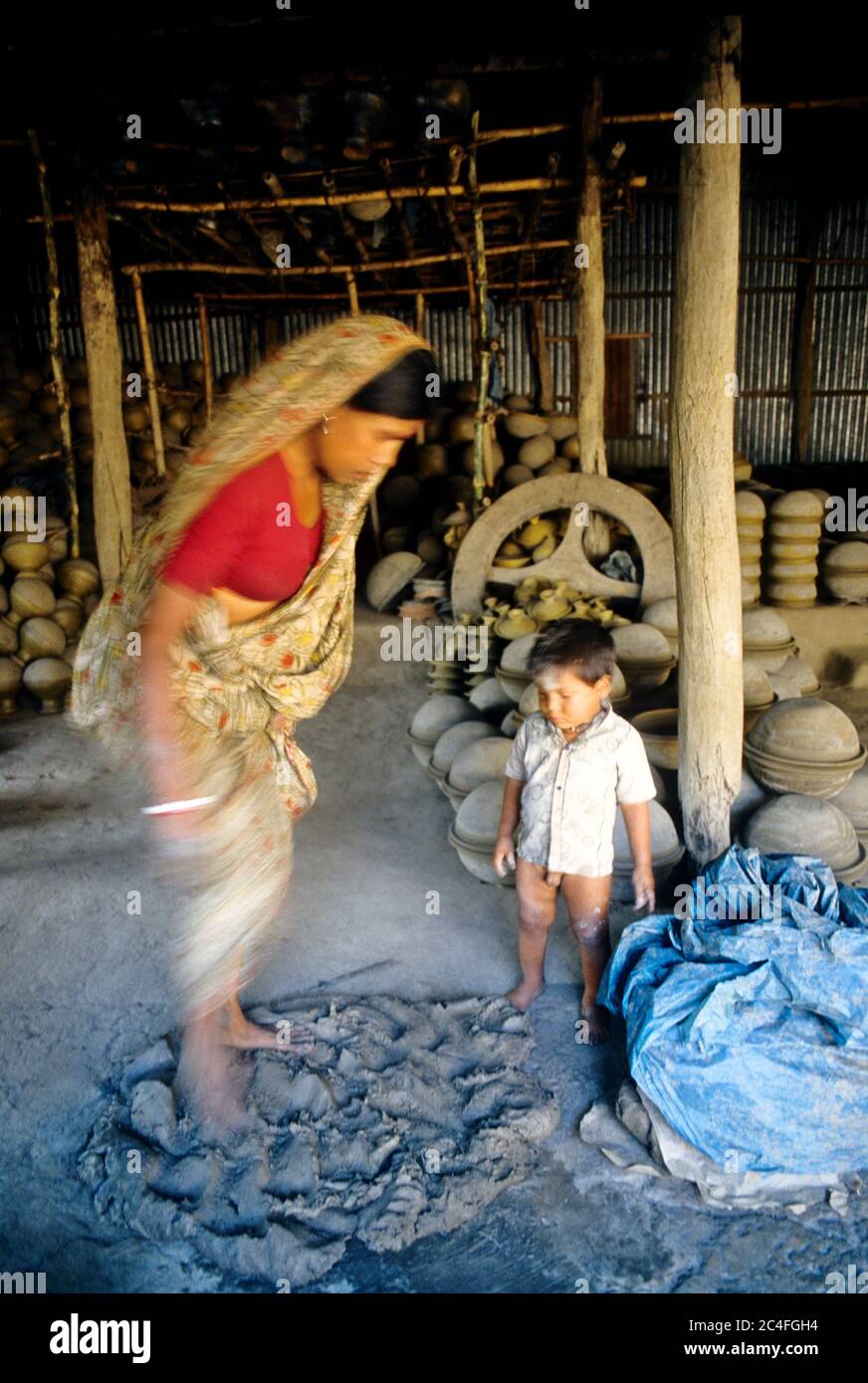 A woman prepares clay for making pottery by stamping it. Fine clay is used in making pottery, an age-old tradition of Bangladesh. Stock Photo