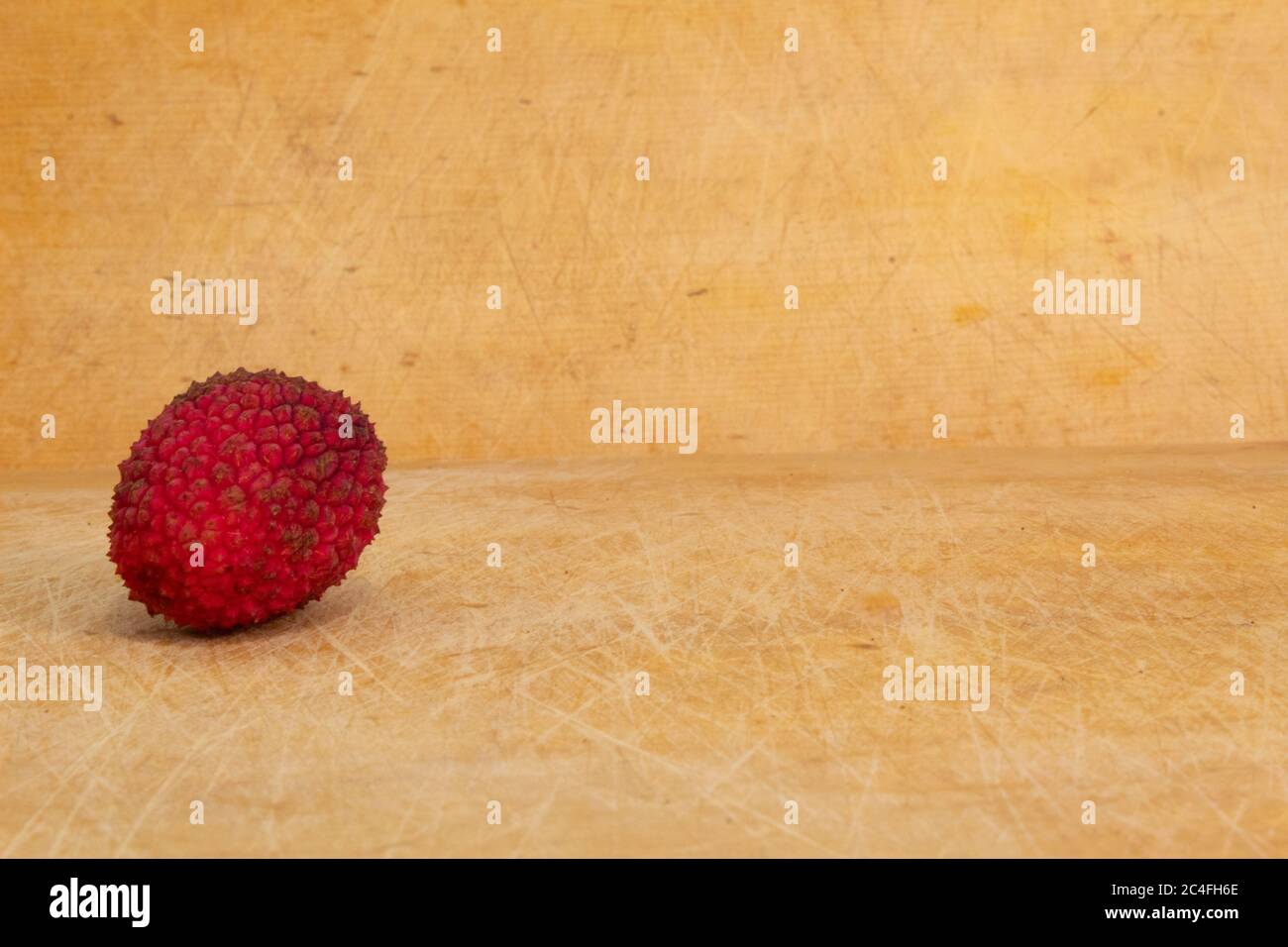 one single red lychee on a wooden colored background Stock Photo