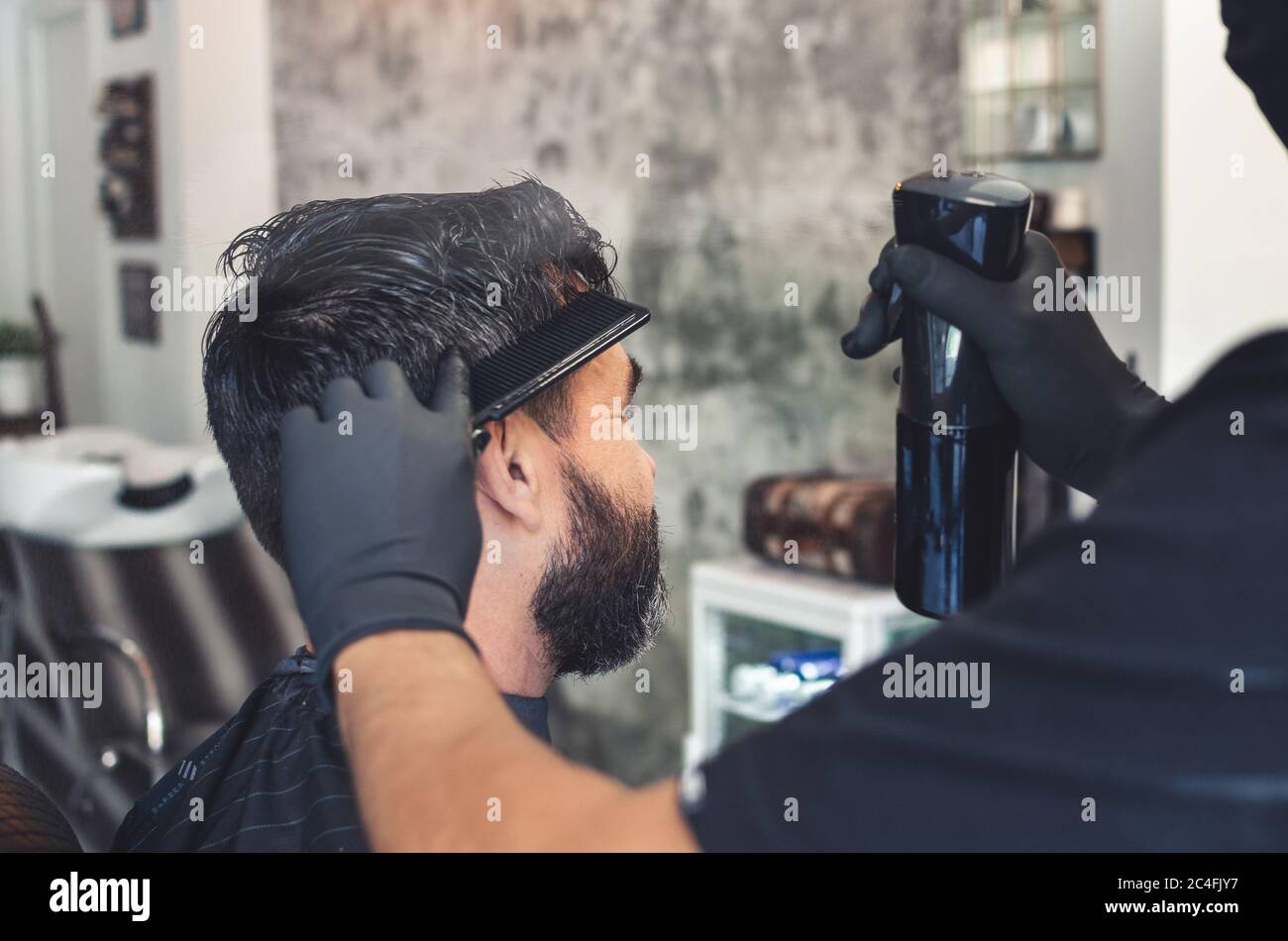 Barber wetting a client's hair with a sprayer from the background Stock Photo