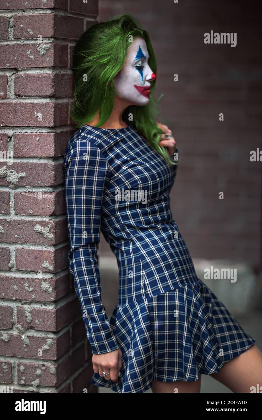 Portrait of a greenhaired girl in chekered dress with joker makeup on a brick wall blurred background. Stock Photo