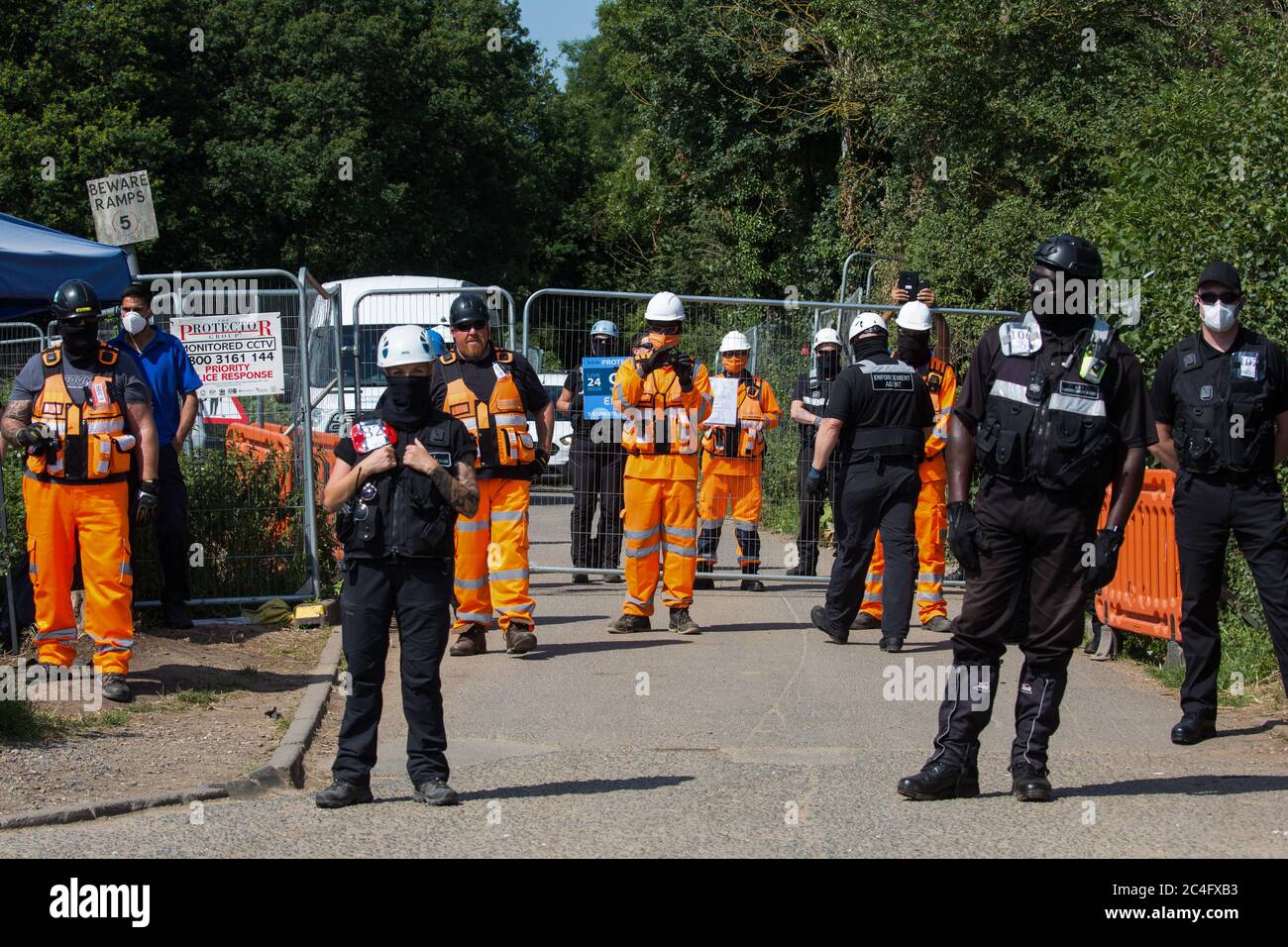 Harefield, UK. 26 June, 2020. HS2 security guards stand in front of a road closure as they observe activists from HS2 Rebellion and Extinction Rebellion UK taking part in a ‘Rebel Trail’ hike along the route of the HS2 high-speed rail link. The activists, who departed from Birmingham on 20th June and will arrive outside Parliament in London on 27th June, are protesting against the environmental impact of the high-speed rail link and questioning the viability of the £100bn+ project. Credit: Mark Kerrison/Alamy Live News Stock Photo