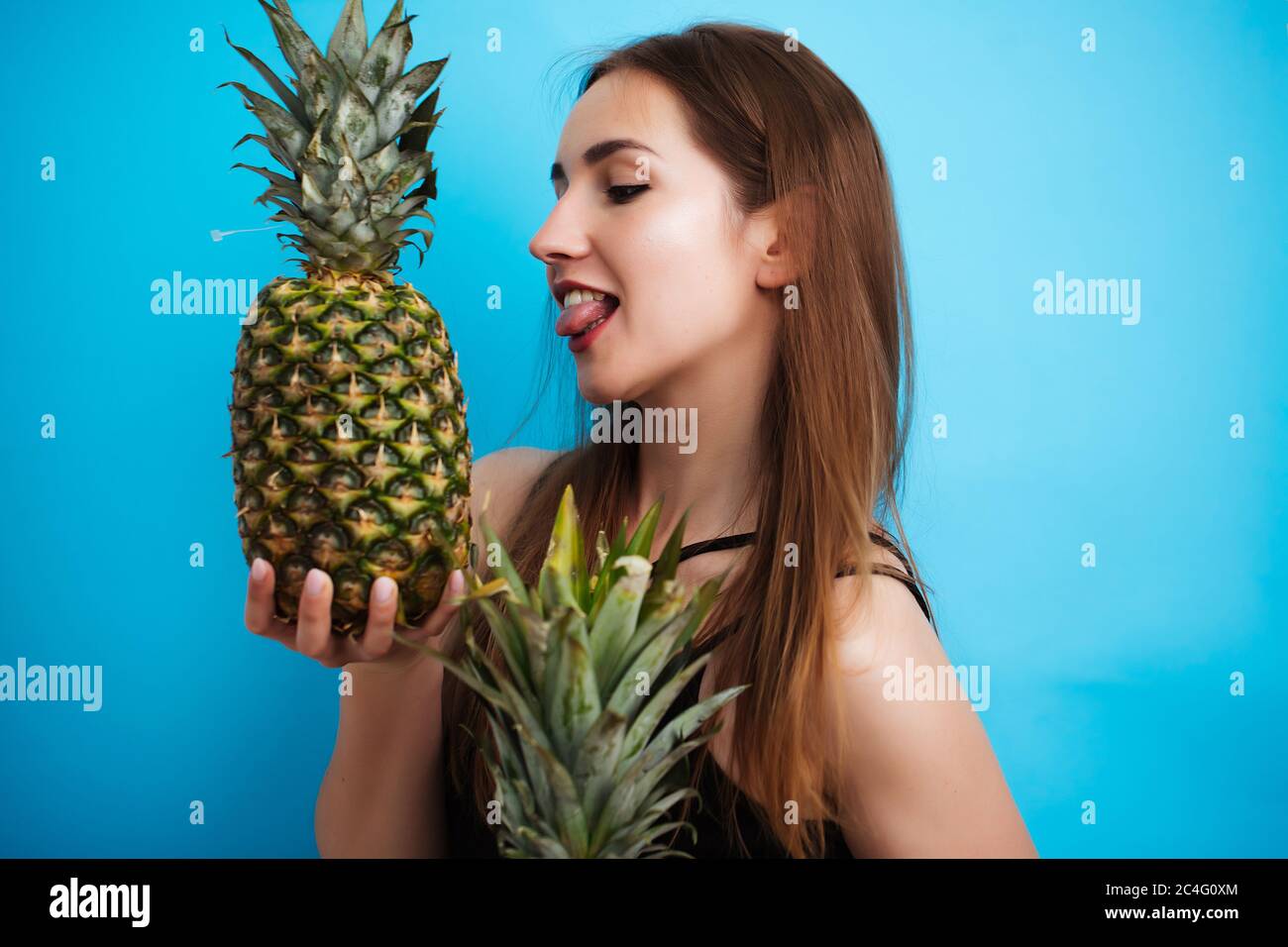 Portrait of young woman in swimsuit with pineapple on blue background. Summer season Stock Photo