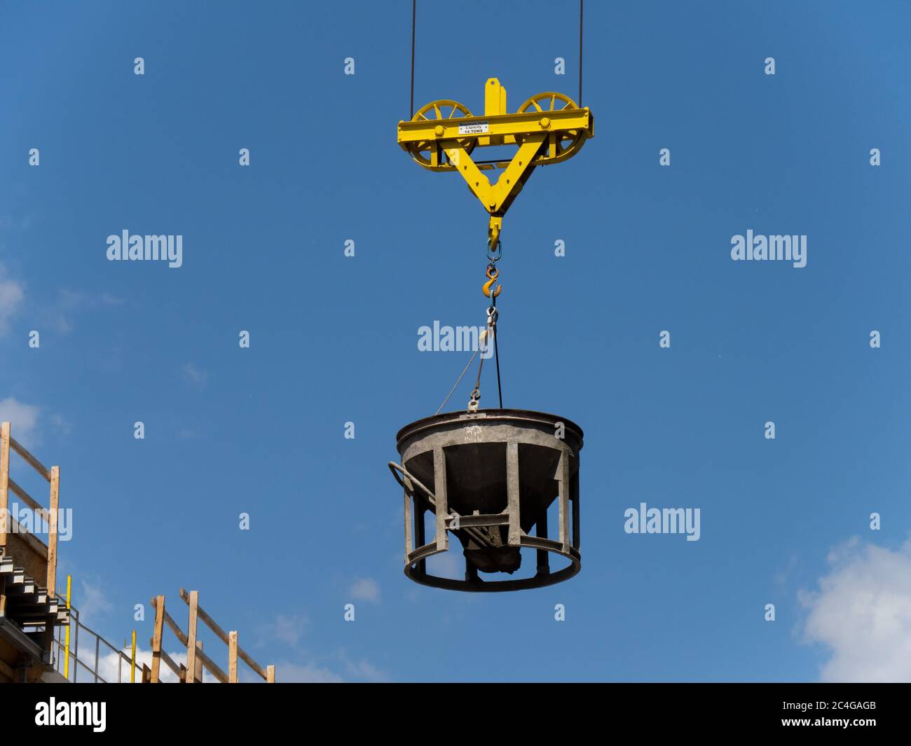 a concrete bucket hanging from a crane at a high rise construction site Stock Photo