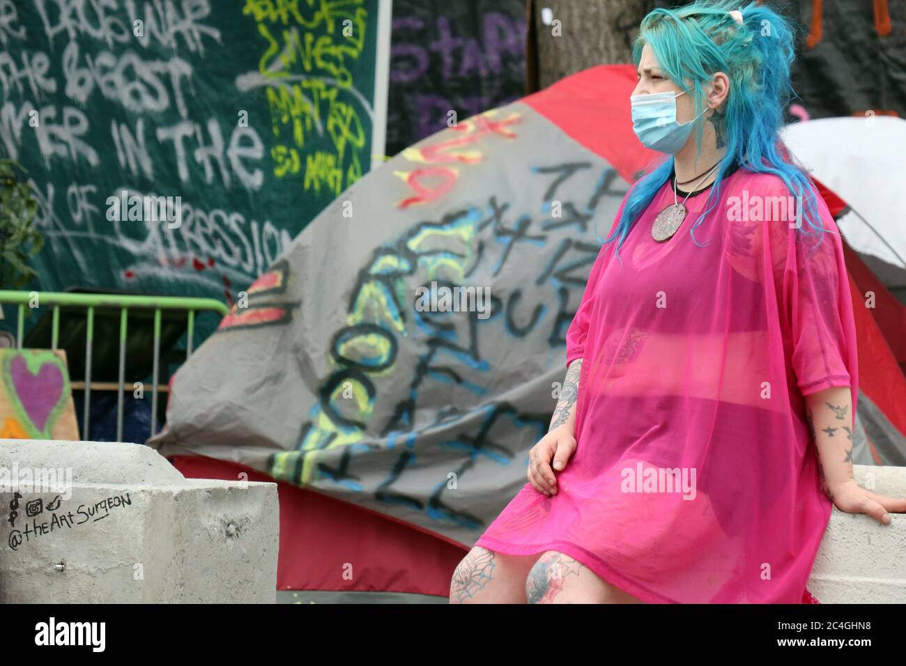 Seattle, United States. 26th June, 2020. A woman sits on a cement block outside the abandoned Seattle police East Precinct station inside the so-called 'Capitol Hill Occupied Protest' zone. This afternoon, Mayor Jenny Durkan met with some protesters to try to negotiate an end to the stand-off. Credit: SOPA Images Limited/Alamy Live News Stock Photo