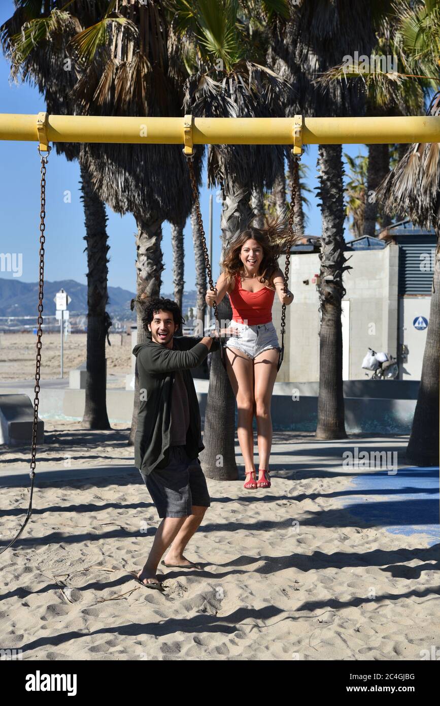 Fun Loving Young Couple Playing On Swings At A Beach Playground Stock