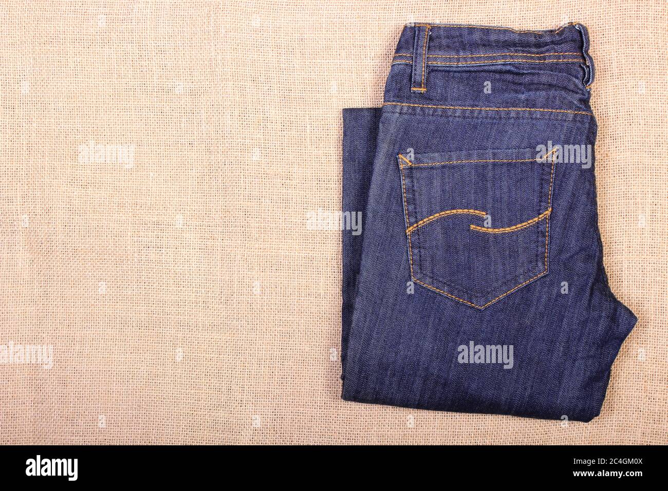 Pair of pants jeans on jute burlap, womanly clothing, place for text or inscription Stock Photo
