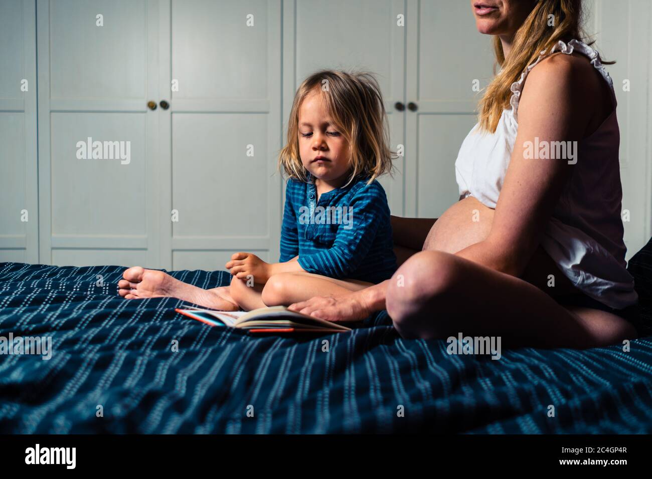 A young pregnant mother is reading to her preschooler on a bed at home Stock Photo