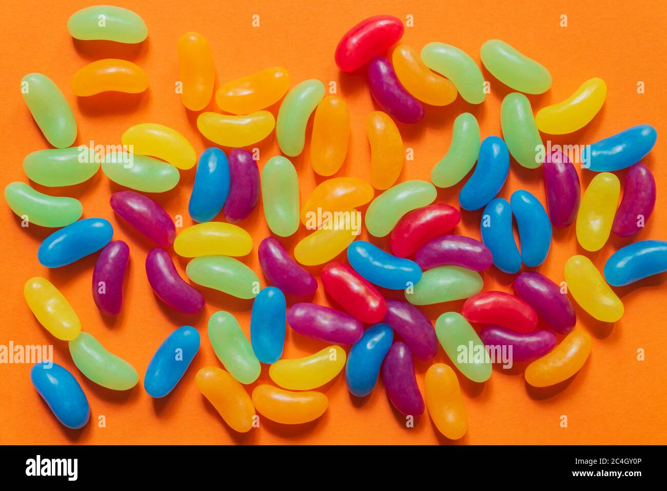 Multi-colored glazed jelly beans sweets on orange paper background. Stock Photo
