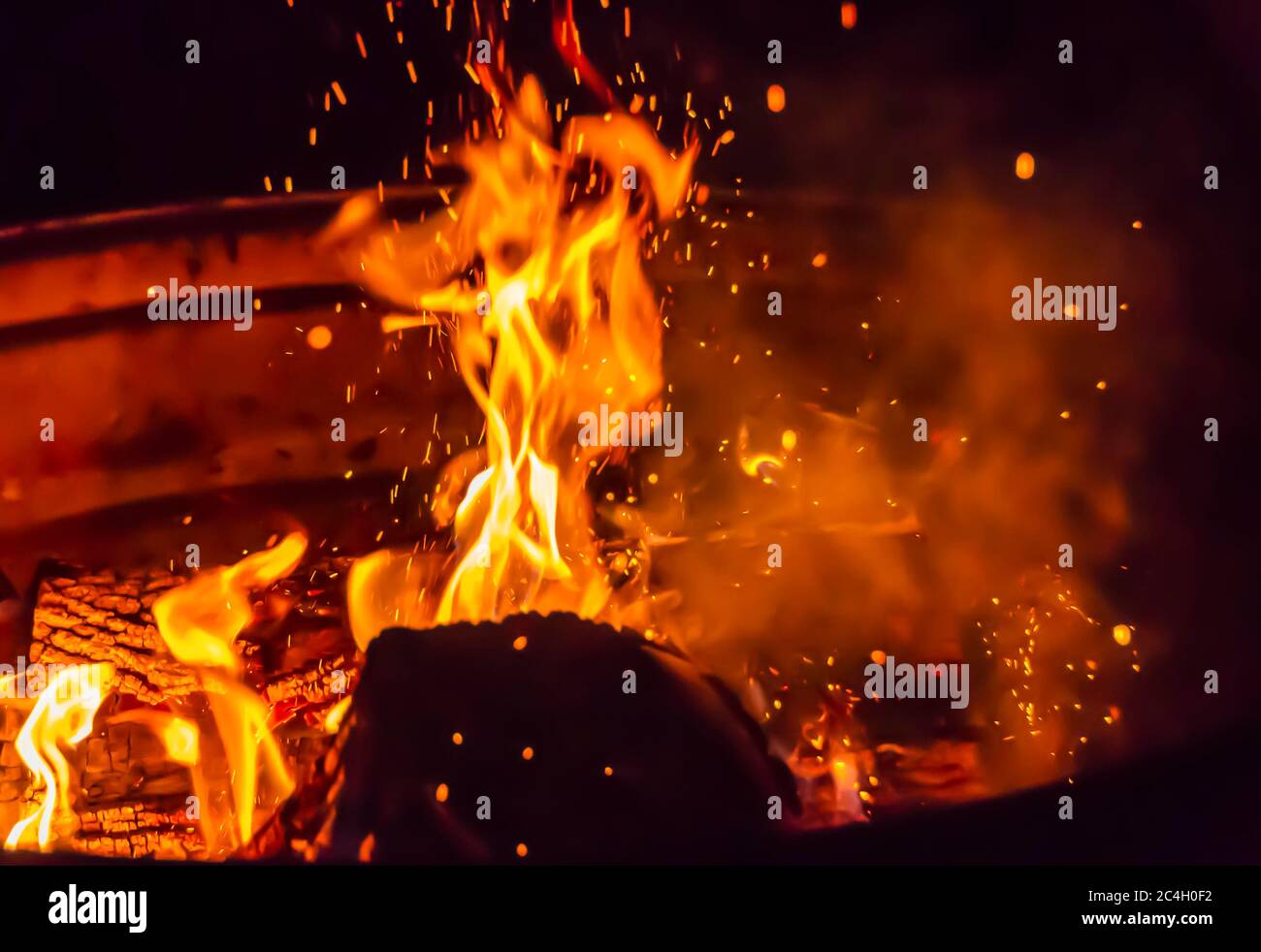 Flames rise from logs being burnt in a bonfire lit inside a metal drum. Stock Photo