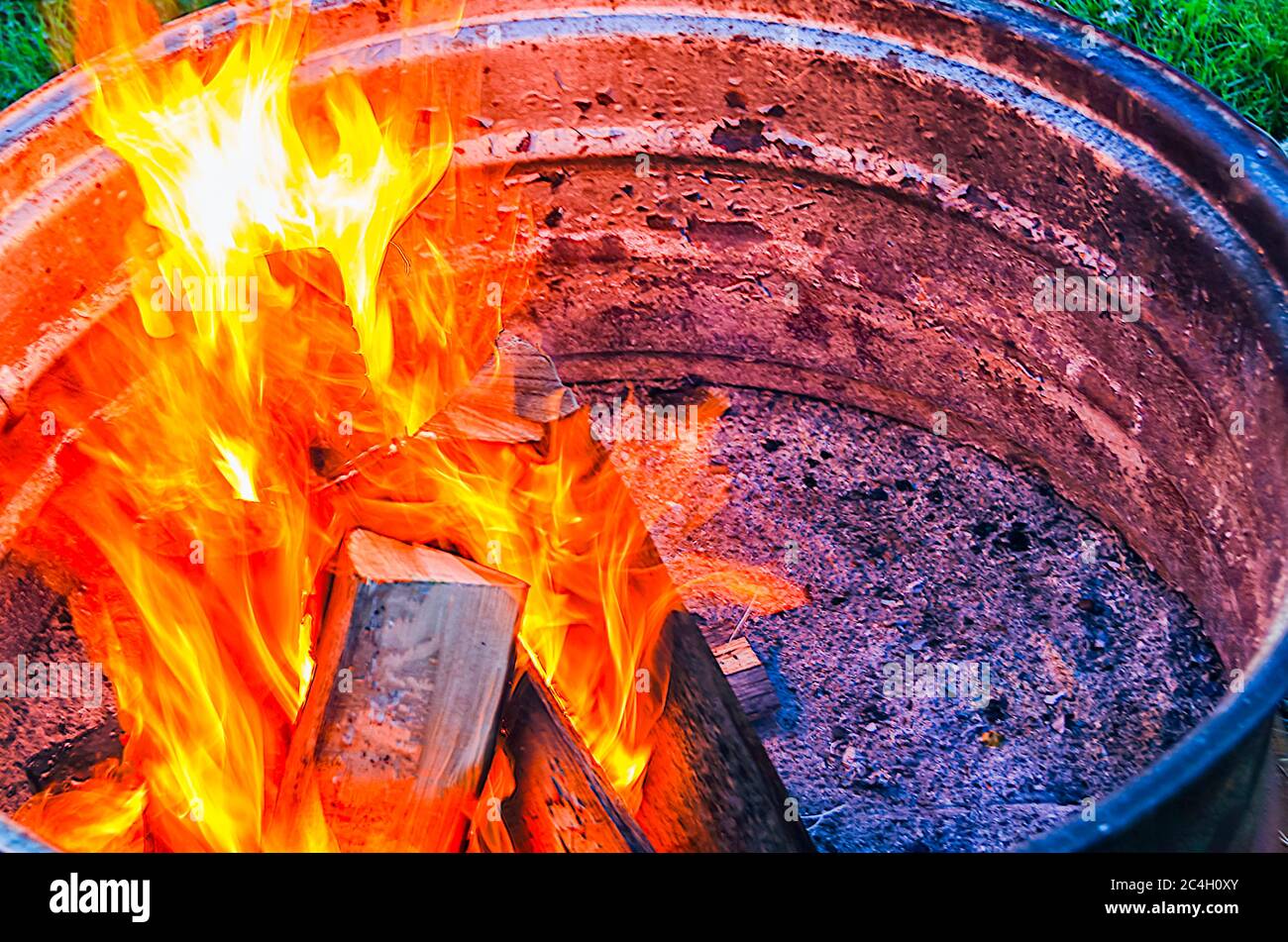 Flames rising from logs being burnt in a bonfire lit inside a metal drum. Stock Photo