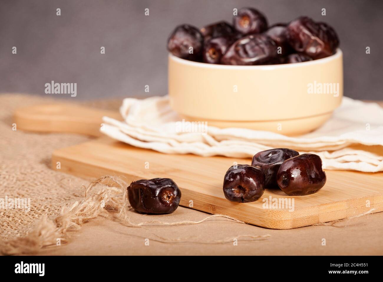 Some dates in a light yellow ceramic bowl and some dates around it on a wooden and sacking surface. Ramadan dates. Stock Photo