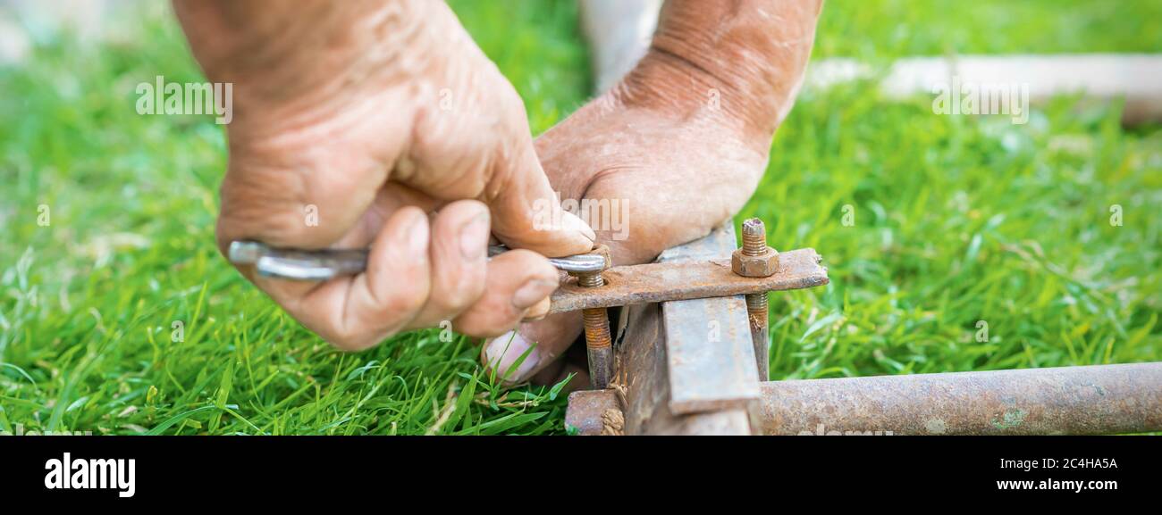 hand of an elderly man twisting the nut with a wrench outdoors. Repair by wrench. Stock Photo