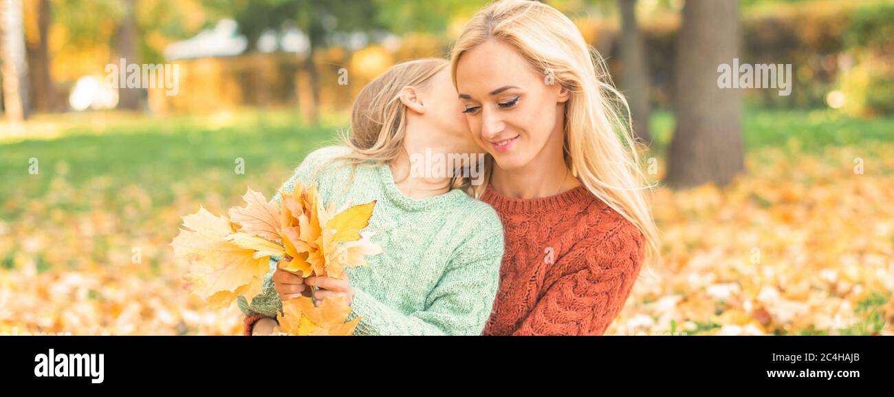 Happy young caucasian mother and little daughter holding autumn yellow leaves sitting and kissing at the park Stock Photo