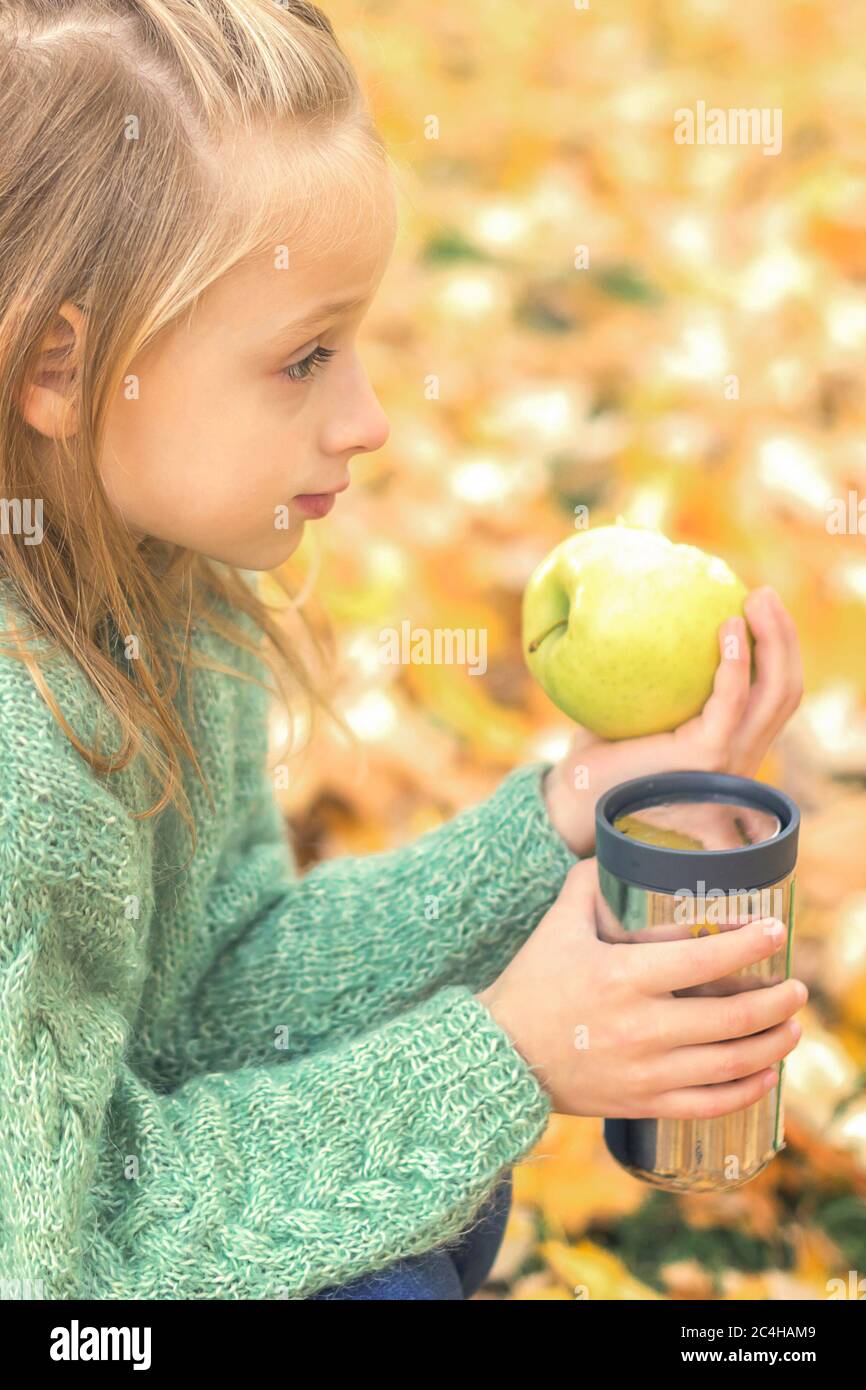 Beautiful little caucasian girl with apple and drink sitting in autumn park Stock Photo