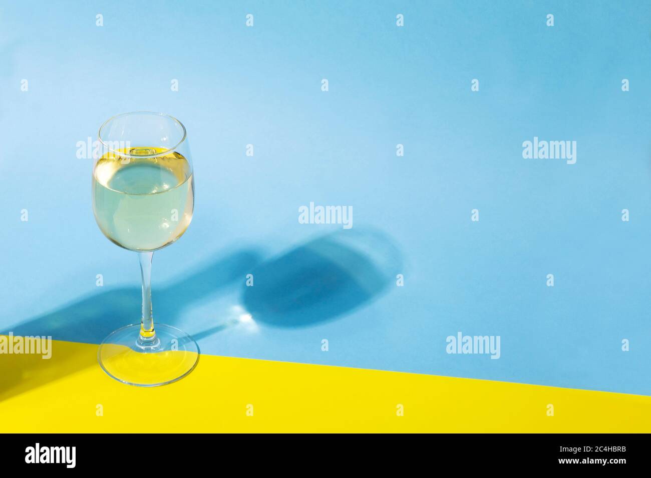 Glass of white wine on yellow blue background, long shadow from the glass and  bottle of wine. Shadow effect, hard light. Copy space Stock Photo