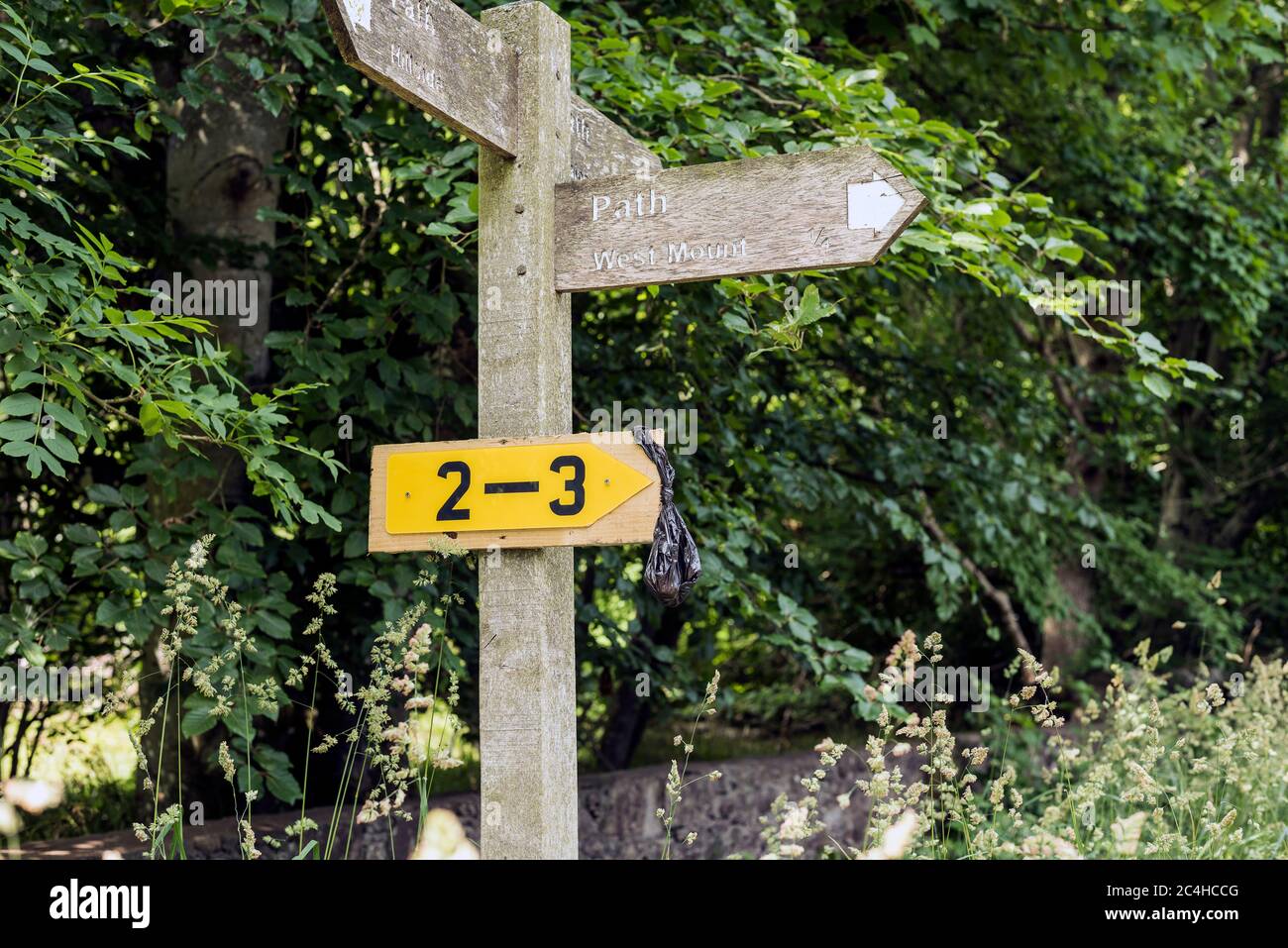 Black plastic dog poo bag hanging from path sign post in rural area of Angus, Scotland. Concept: selfish, litter, moronic, inconsiderate, ignorance, Stock Photo