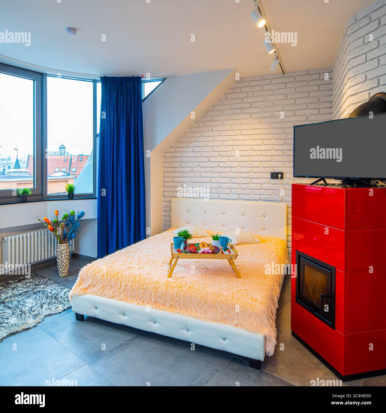 Modern loft interior of luxury studio apartment. Brick wall. Panorama window. Tray with food on the bed. TV on the fireplace. Stock Photo
