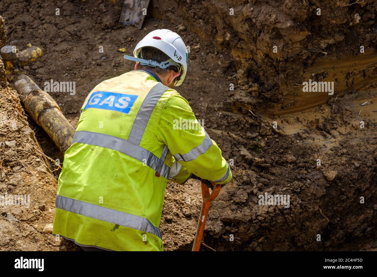 Gas engineer digs around pipe in trench on construction site Stock Photo