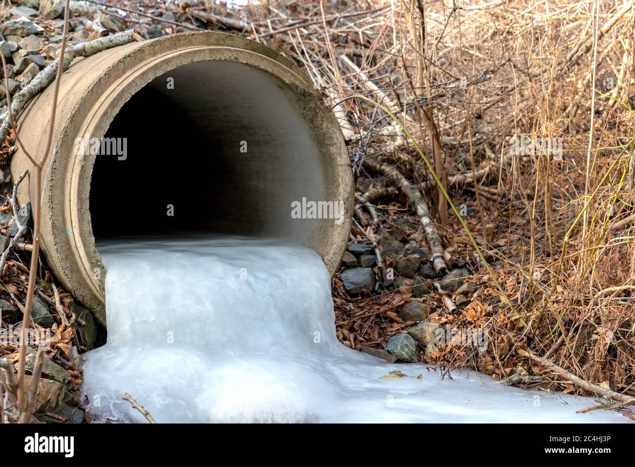 Looking into a frozen culvert. The pipe is about a quarter full of ice which flows out the end. Stock Photo