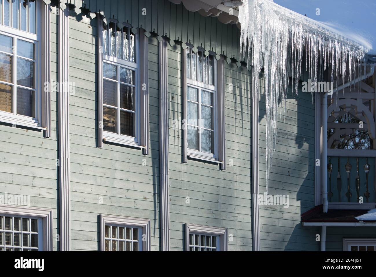 Ice stalactite hanging from the roof with wooden wall. Building covered with large icicles. Icicles are very dangerous for life. Poor thermal insulati Stock Photo