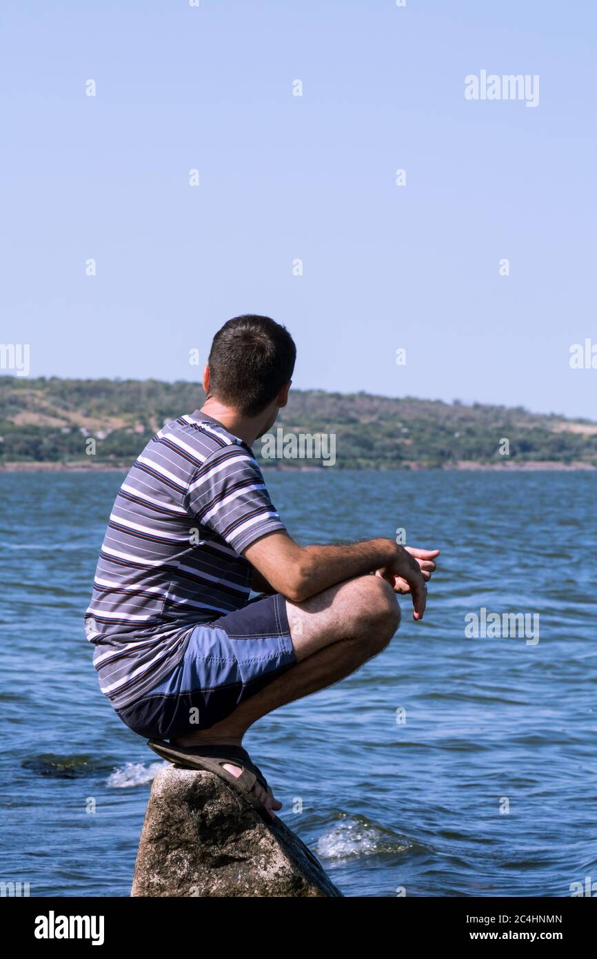 The young man relaxing sitting on a rock near the sea Stock Photo