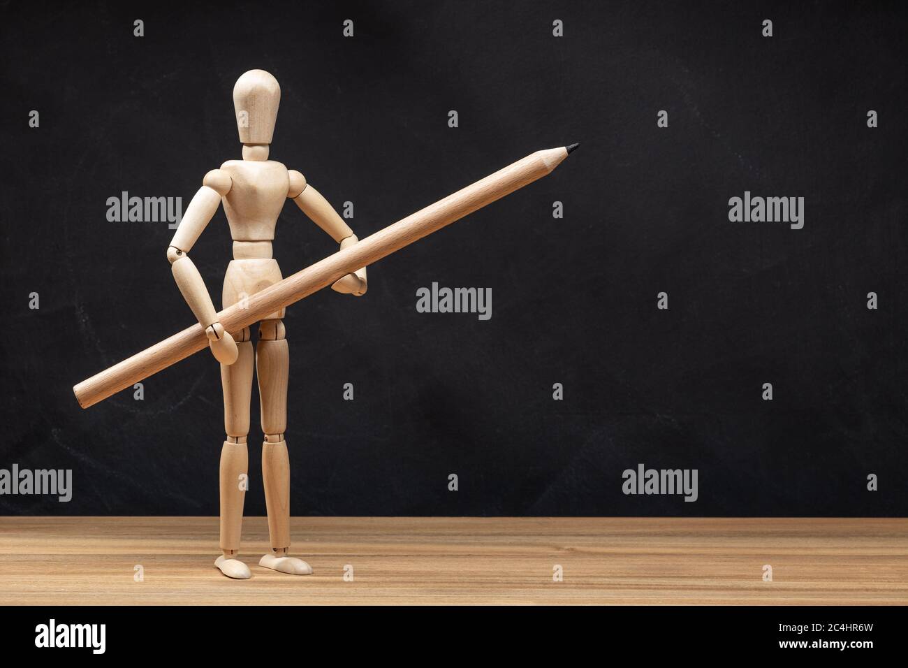 Wooden mannequin holding a pencil. Blackboard background. Drawing concept. Copy space Stock Photo