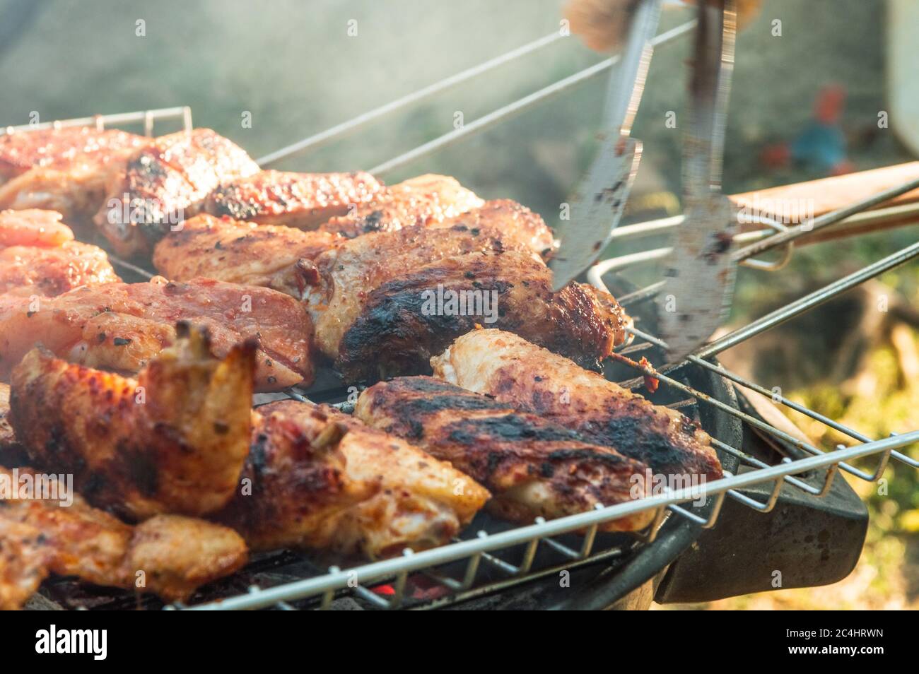 Flipping a barbecued chicken meat with tongs on a charcoal barbeque grill. Tasty snack party. Stock Photo