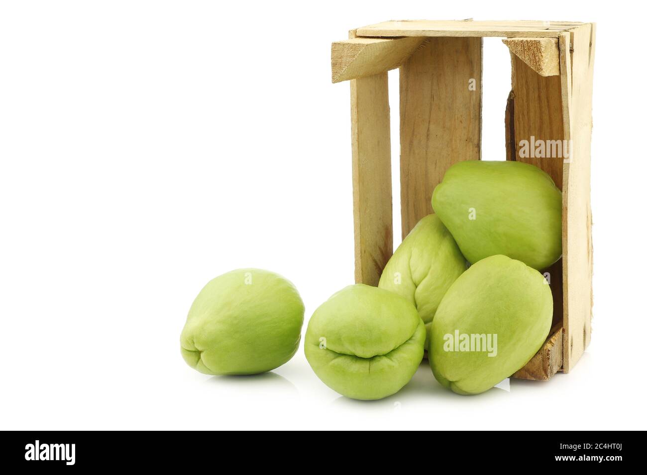 Chayote fruit (Sechium edulis)and a cut one in a wooden crate on a white background Stock Photo