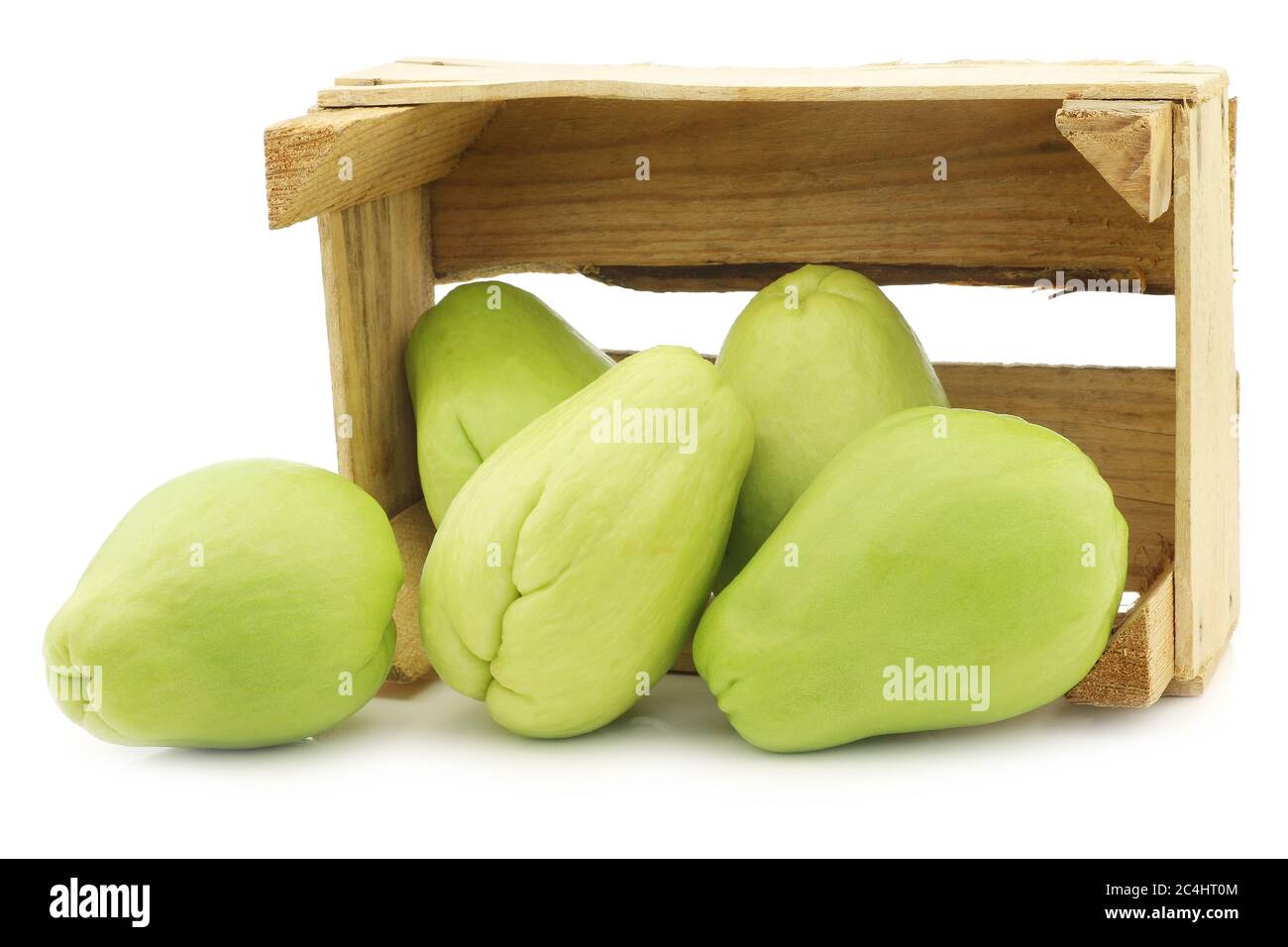 Chayote fruit (Sechium edulis)and a cut one in a wooden crate on a white background Stock Photo