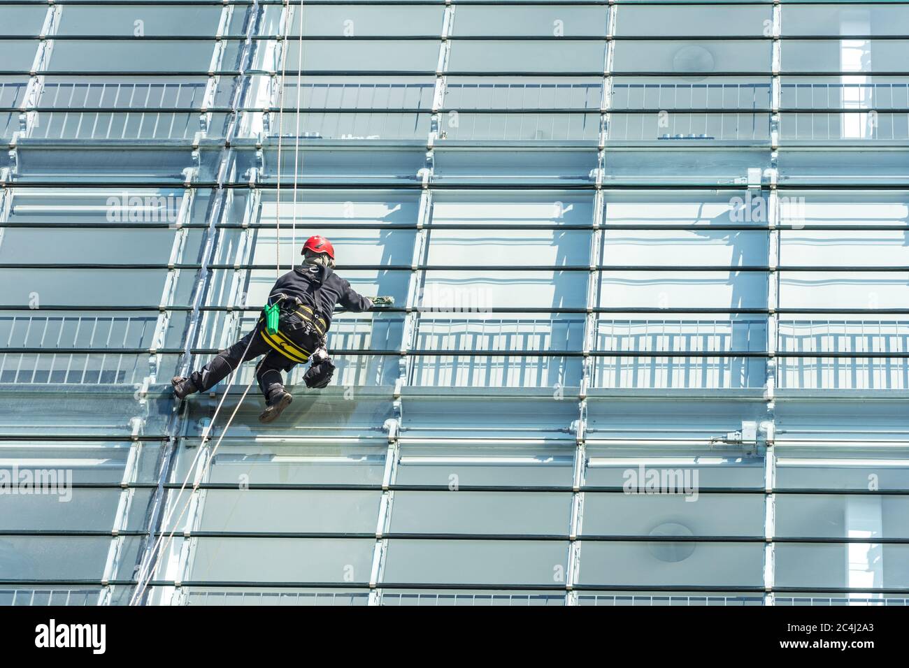 Window cleaner with safety equipment on the shiny glass facade of a skyscraper Stock Photo