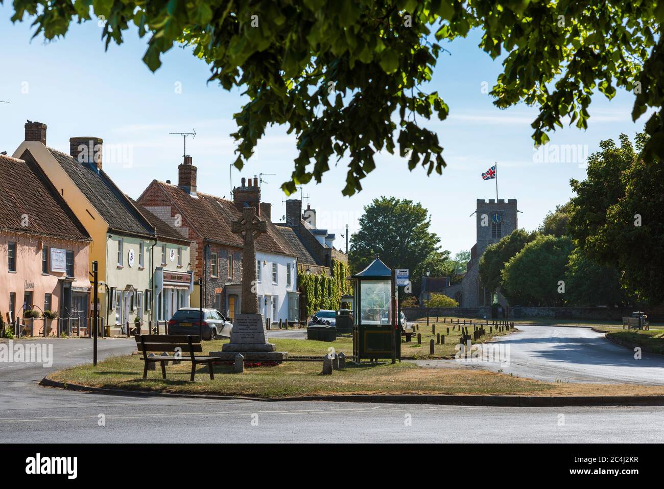 Village street UK, view in summer of the war memorial cross and traditional shops on The Green in Burnham Market, north Norfolk, UK. Stock Photo