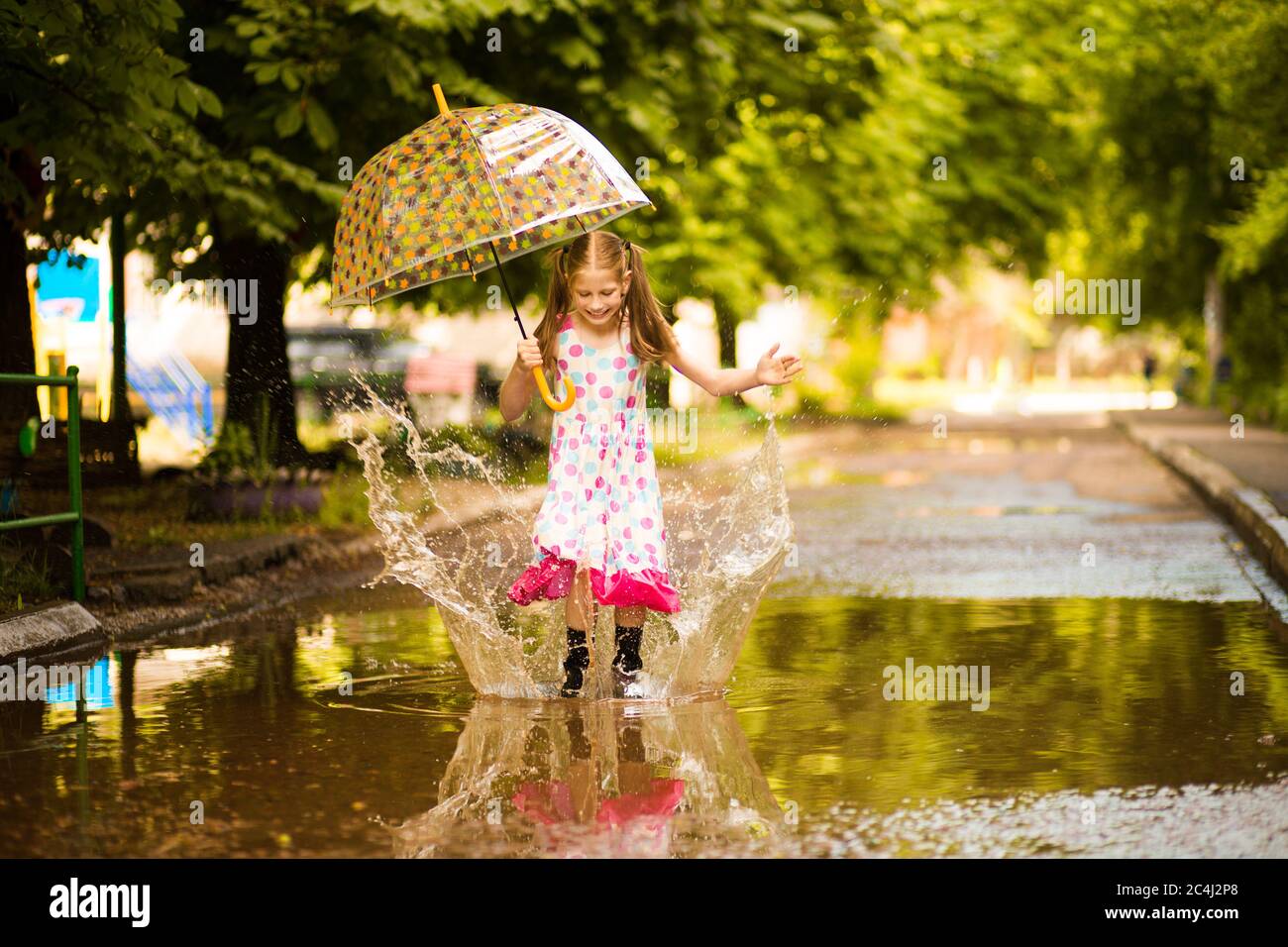 Happy funny kid girl with umbrella jumping on puddles in rubber boots ...
